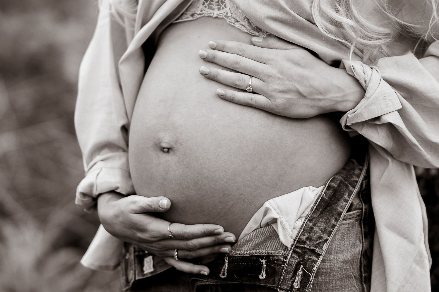 Black and white close-up of pregnant woman cradling baby bump with both hands.