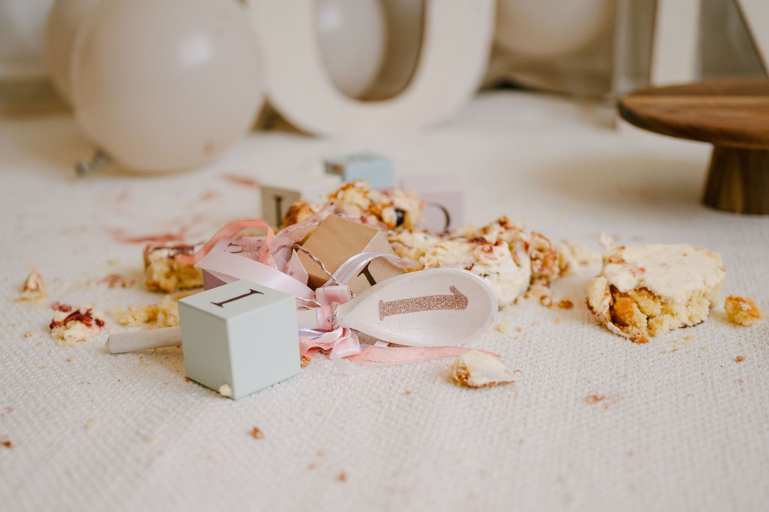 Smashed birthday cake scattered on white floor with pink ribbons and decorative elements during cake smash photoshoot.