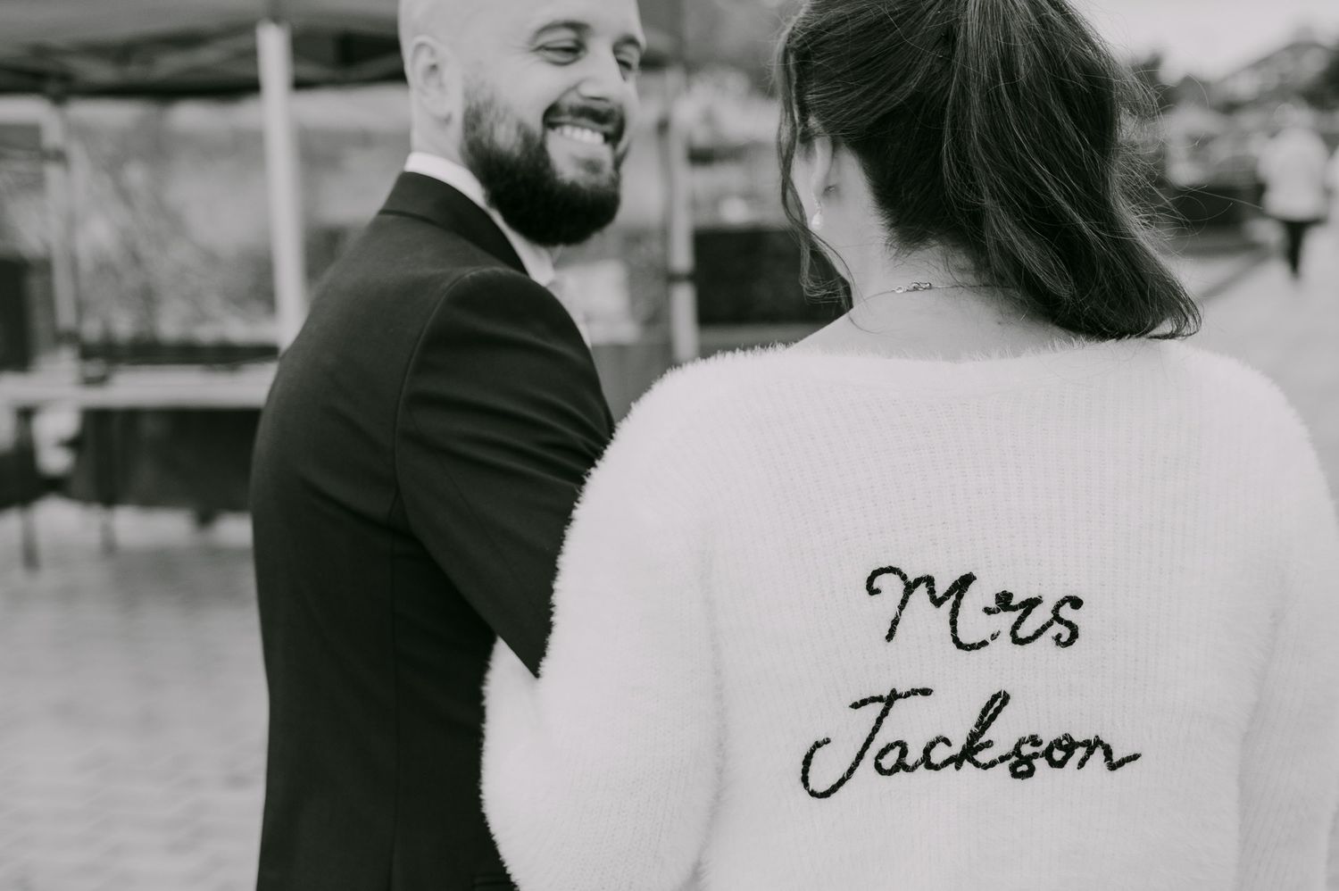 Black and white photo of bride in Mrs Jackson embroidered sweater smiling with her groom at their wedding.