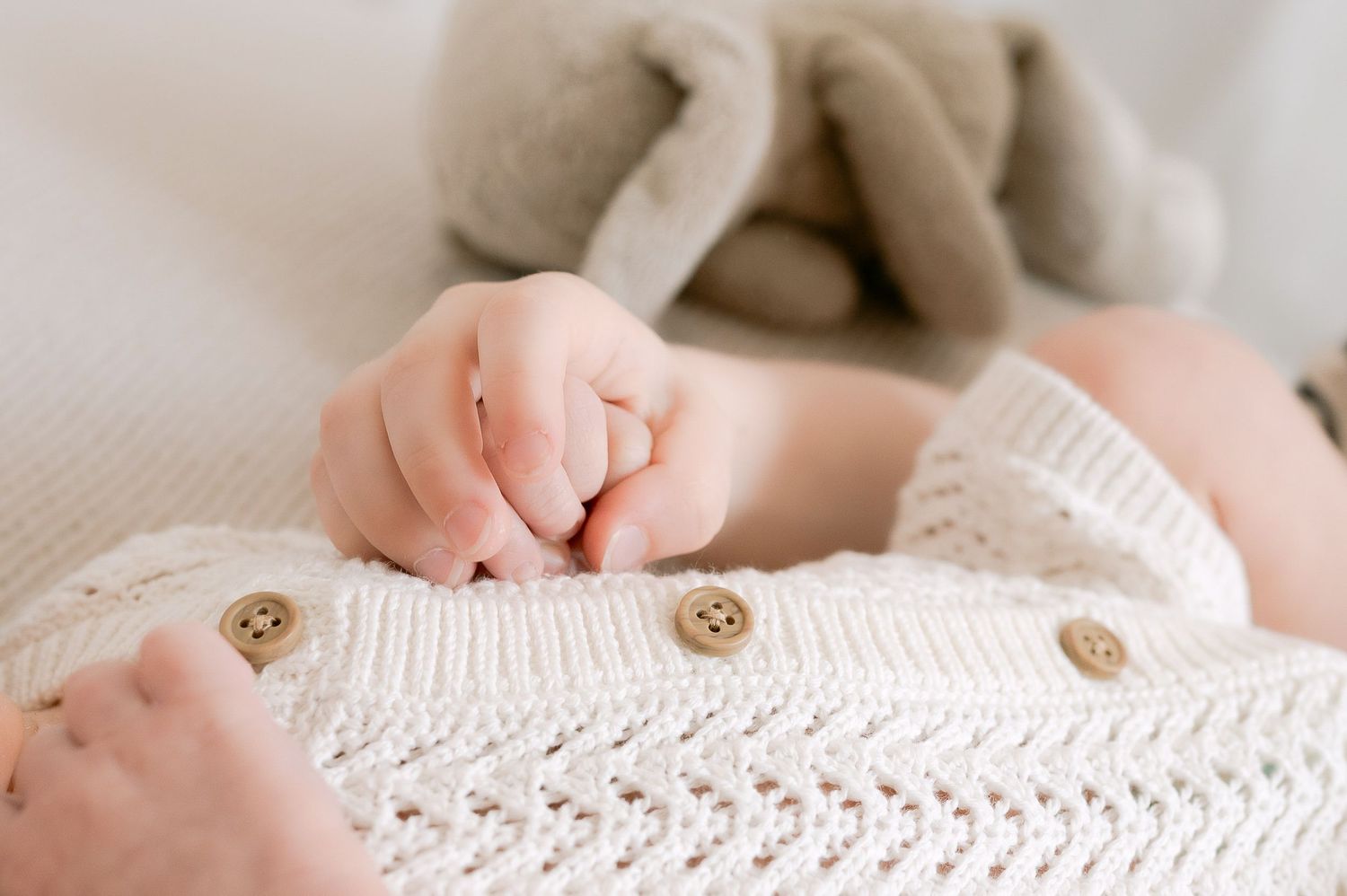 Close-up of newborn baby fists on cream knit outfit with wooden buttons.