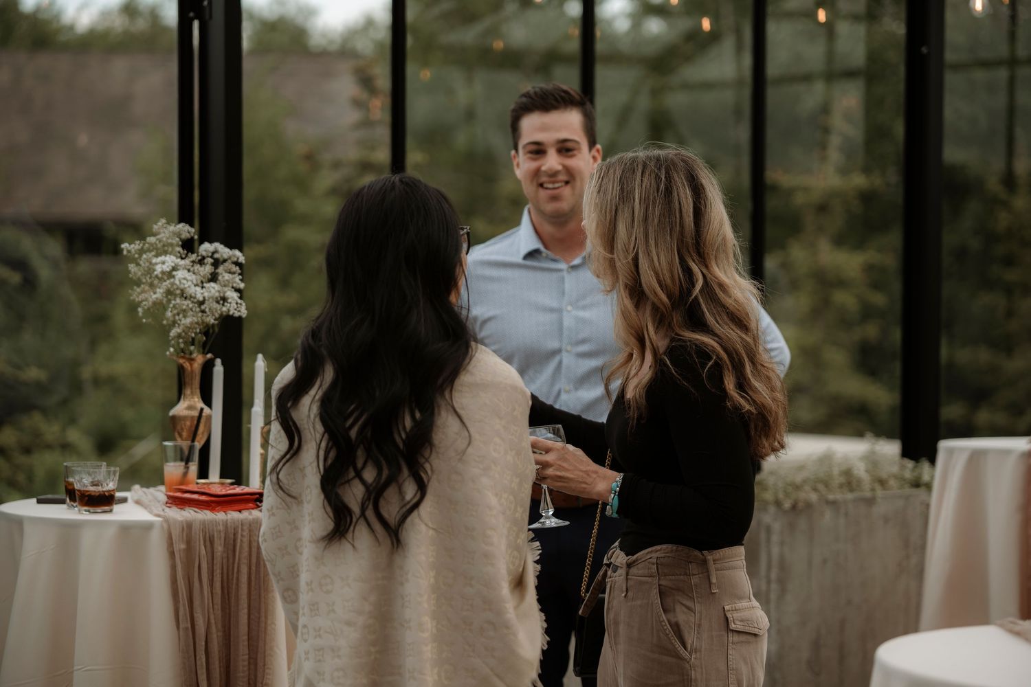 Man in blue shirt smiling and conversing with two women at an elegant indoor event venue.