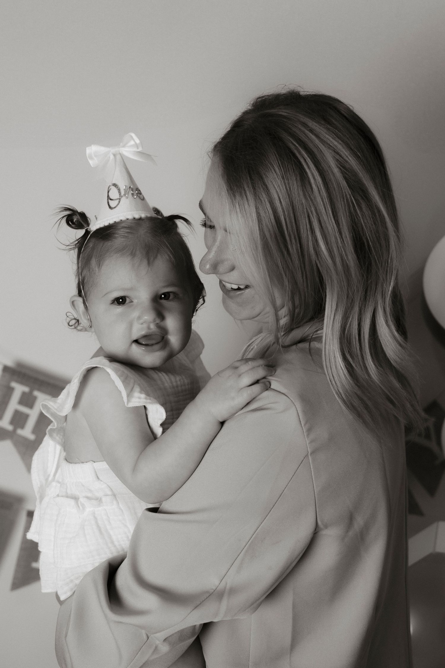 Black and white photo of a mother holding her baby girl wearing a birthday hat at a first birthday party.Family photography in Regina Sask.