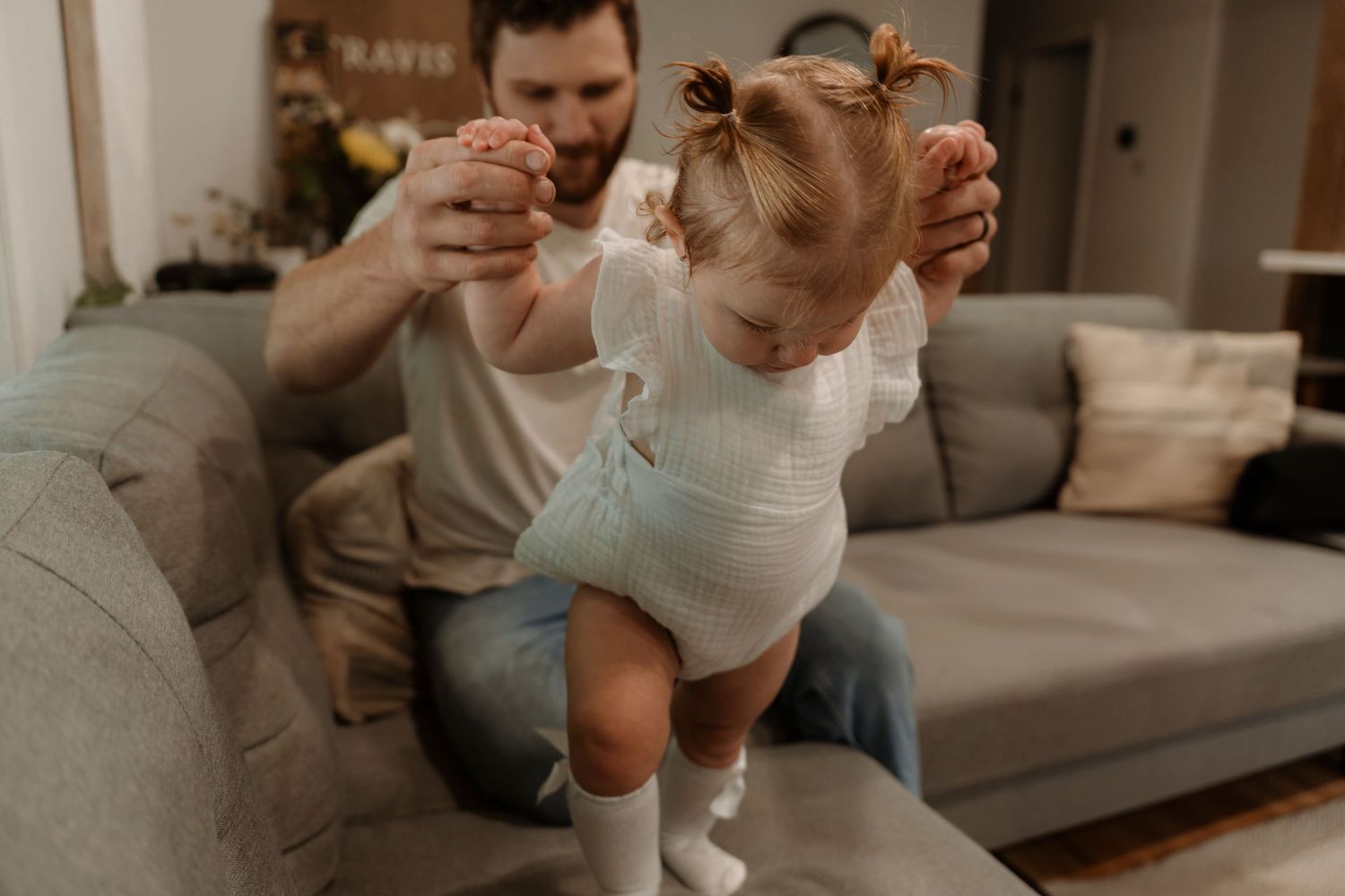 Father helping his toddler daughter take her first steps in a cozy living room.Family photography in Regina Saskatchewan.