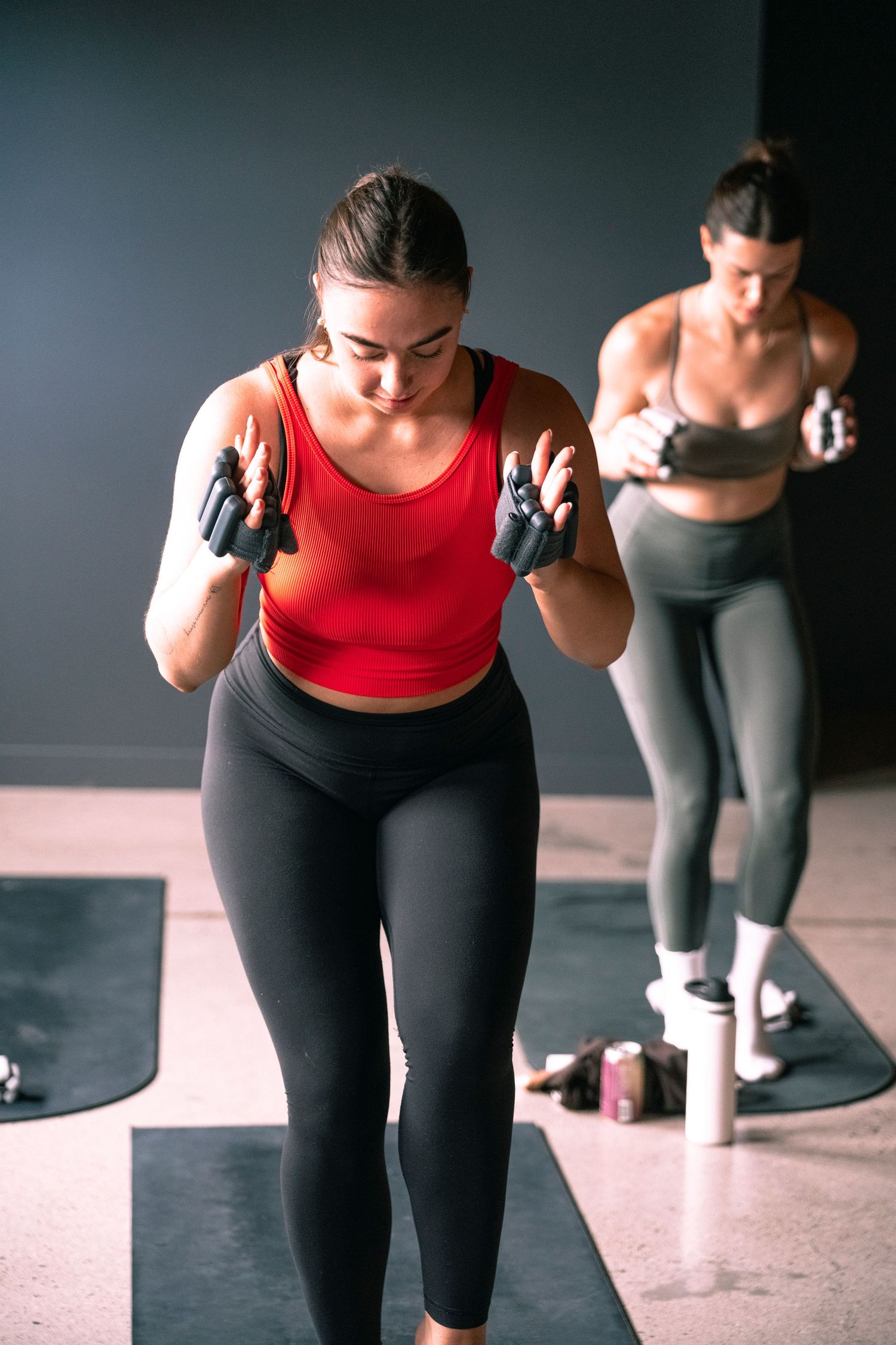 Two women in athletic wear practicing boxing exercises with gloves in a modern gym setting.