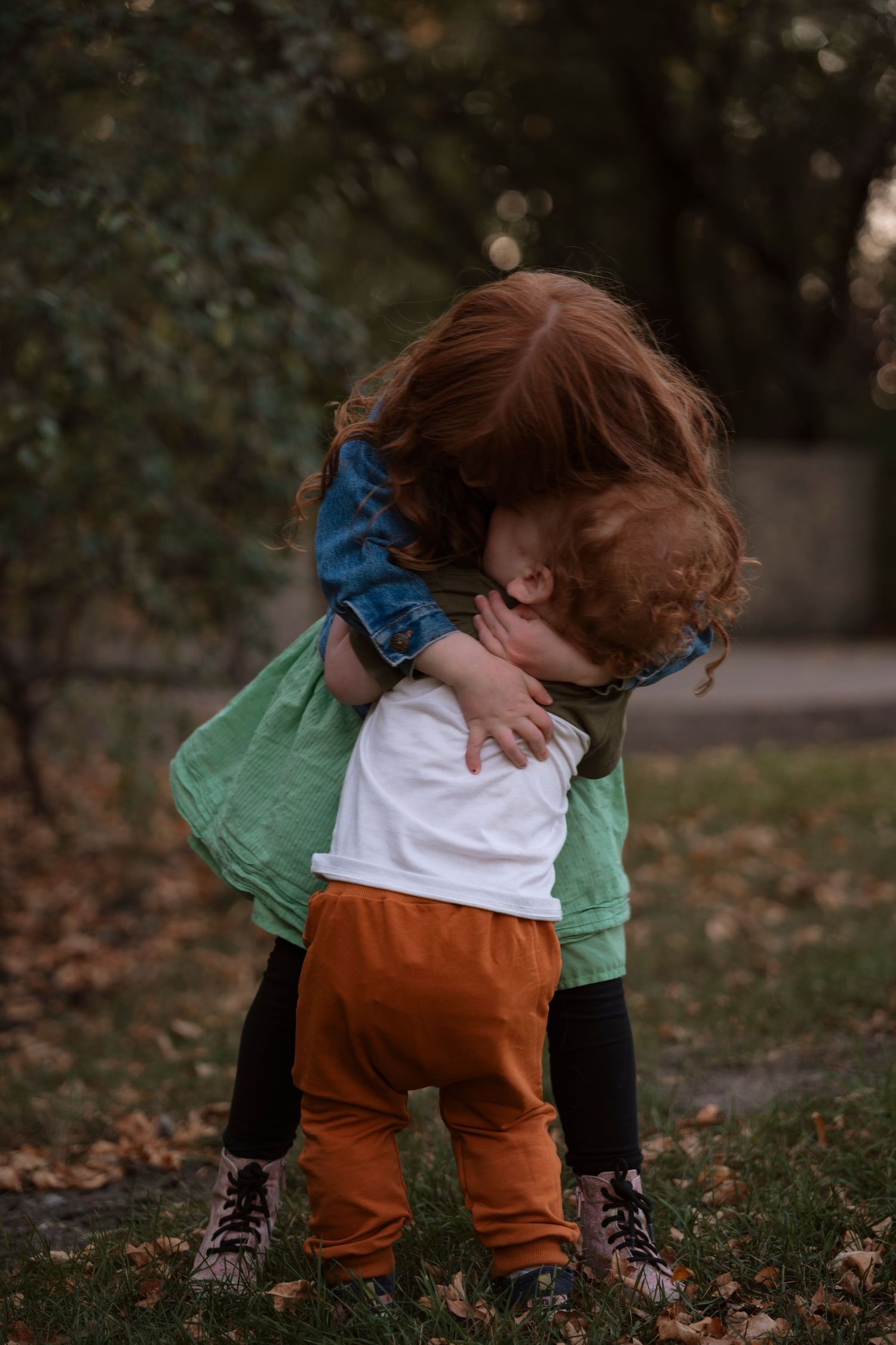 Two young red-haired children share a sweet hug outdoors among autumn fallen leaves. Family photography in Regina Saskatchewan.