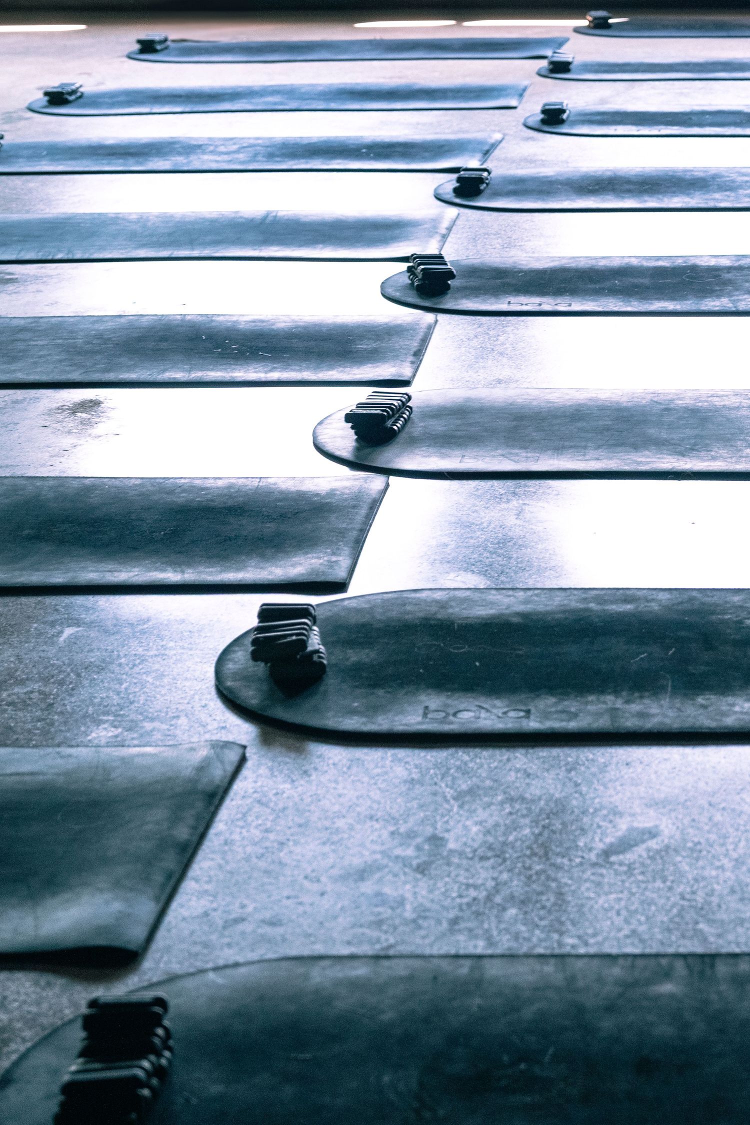 Rows of gray yoga mats with blocks neatly arranged on a studio floor, illuminated by soft natural light.