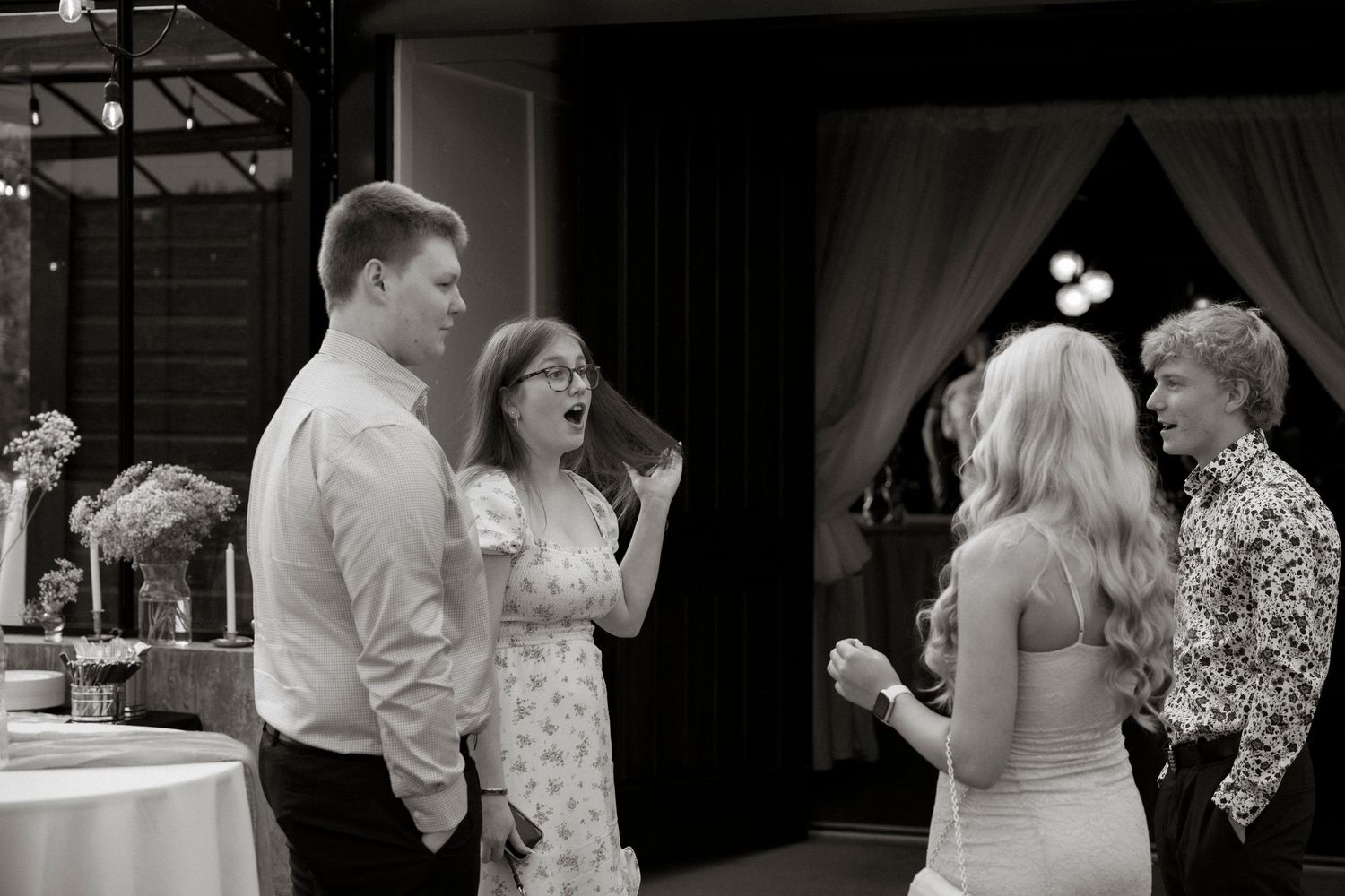 Black and white photo of guests laughing and conversing at an elegant wedding reception venue.