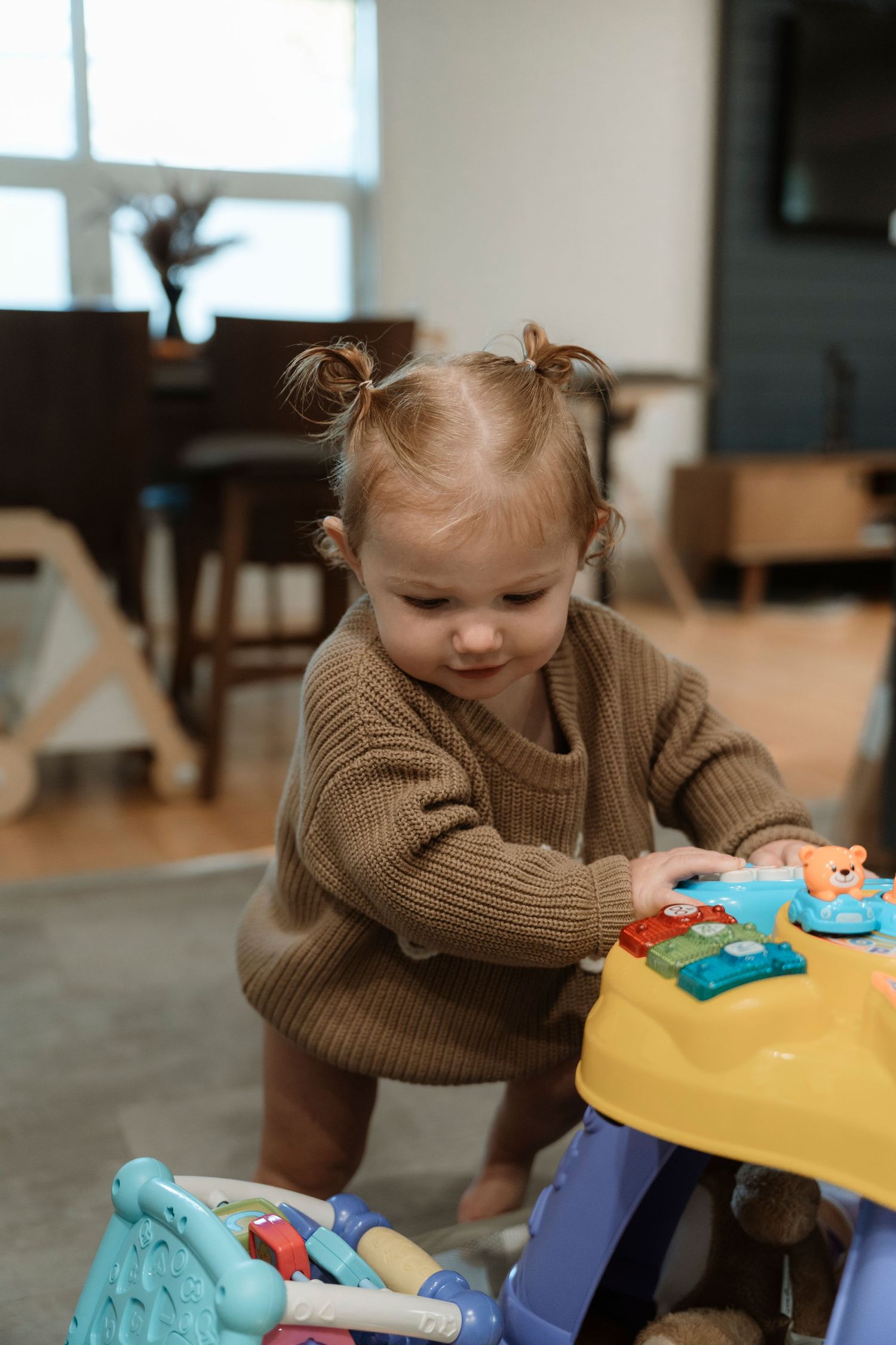 Toddler girl in brown sweater playing with colorful activity toy on living room floor.Family photography in Regina Saskatchewan.