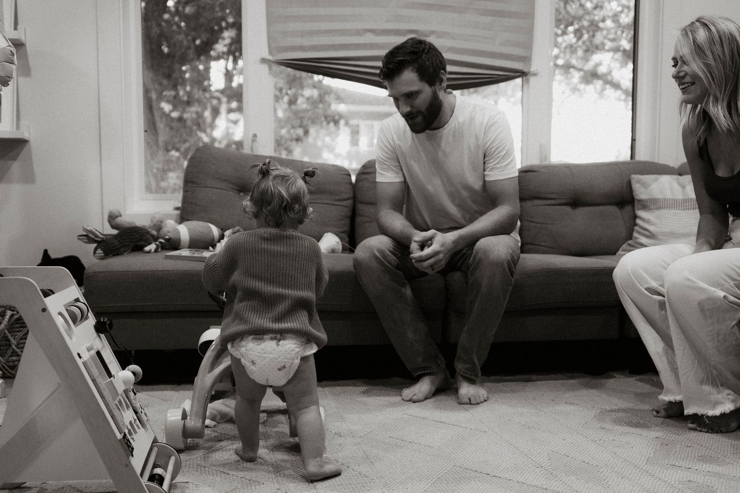 Black and white family photo of parents interacting with their toddler in a cozy living room.Family photography in Regina Saskatchewan.