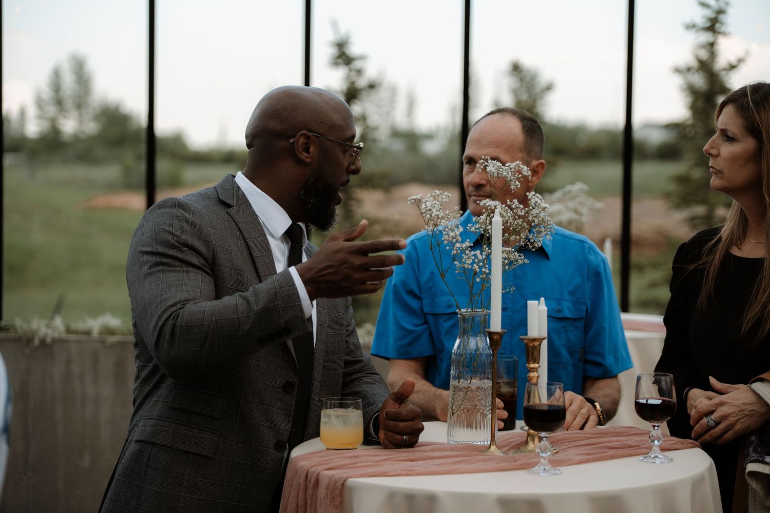 Three people conversing at a round table with candles and wine glasses at an elegant indoor event.