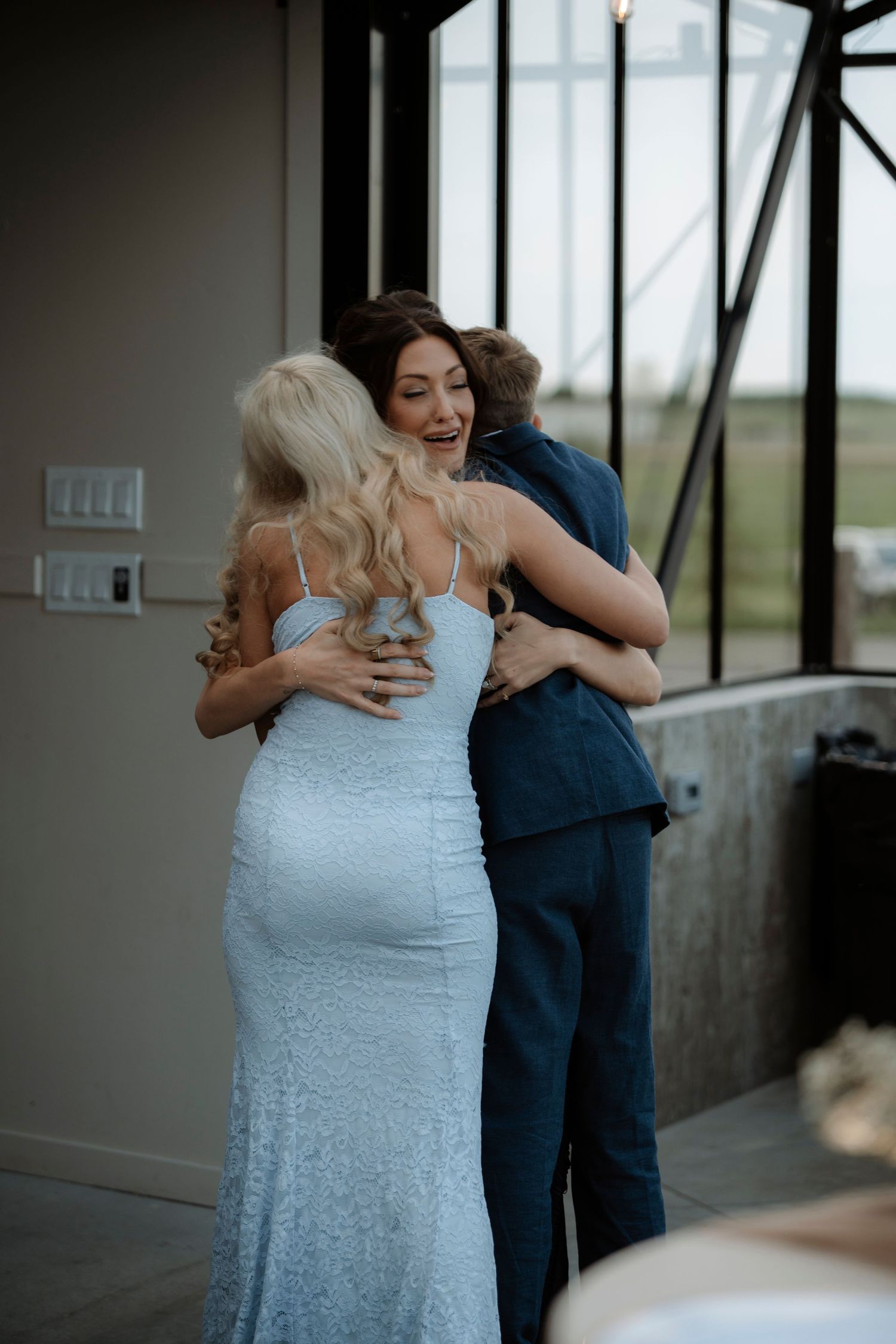 A bride in a light blue gown shares a warm group hug with guests at an elegant indoor wedding venue.