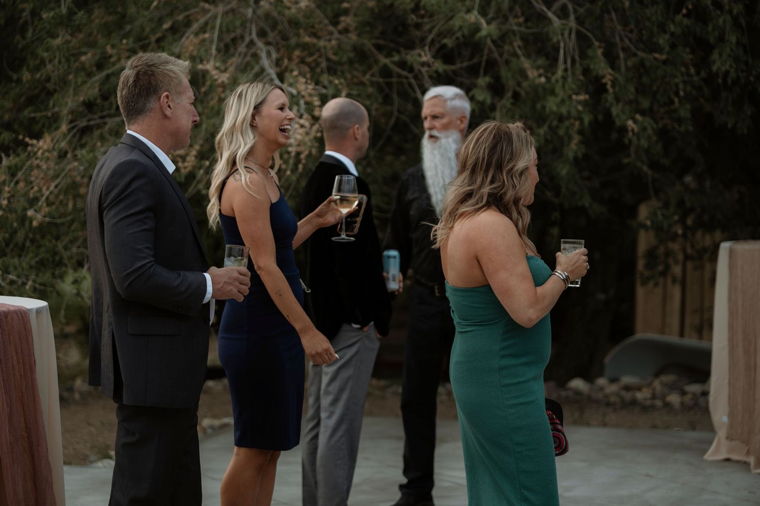 Guests in formal attire socializing outdoors at a wedding reception, holding champagne glasses.