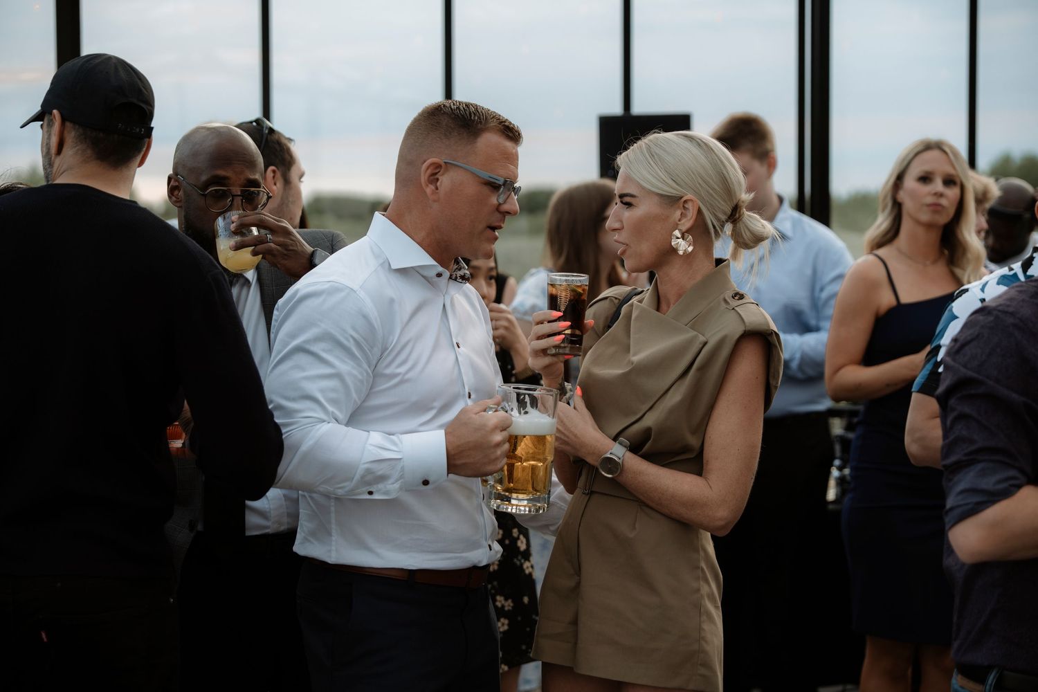 Two professionals networking at an outdoor rooftop event, holding drinks and engaged in conversation.