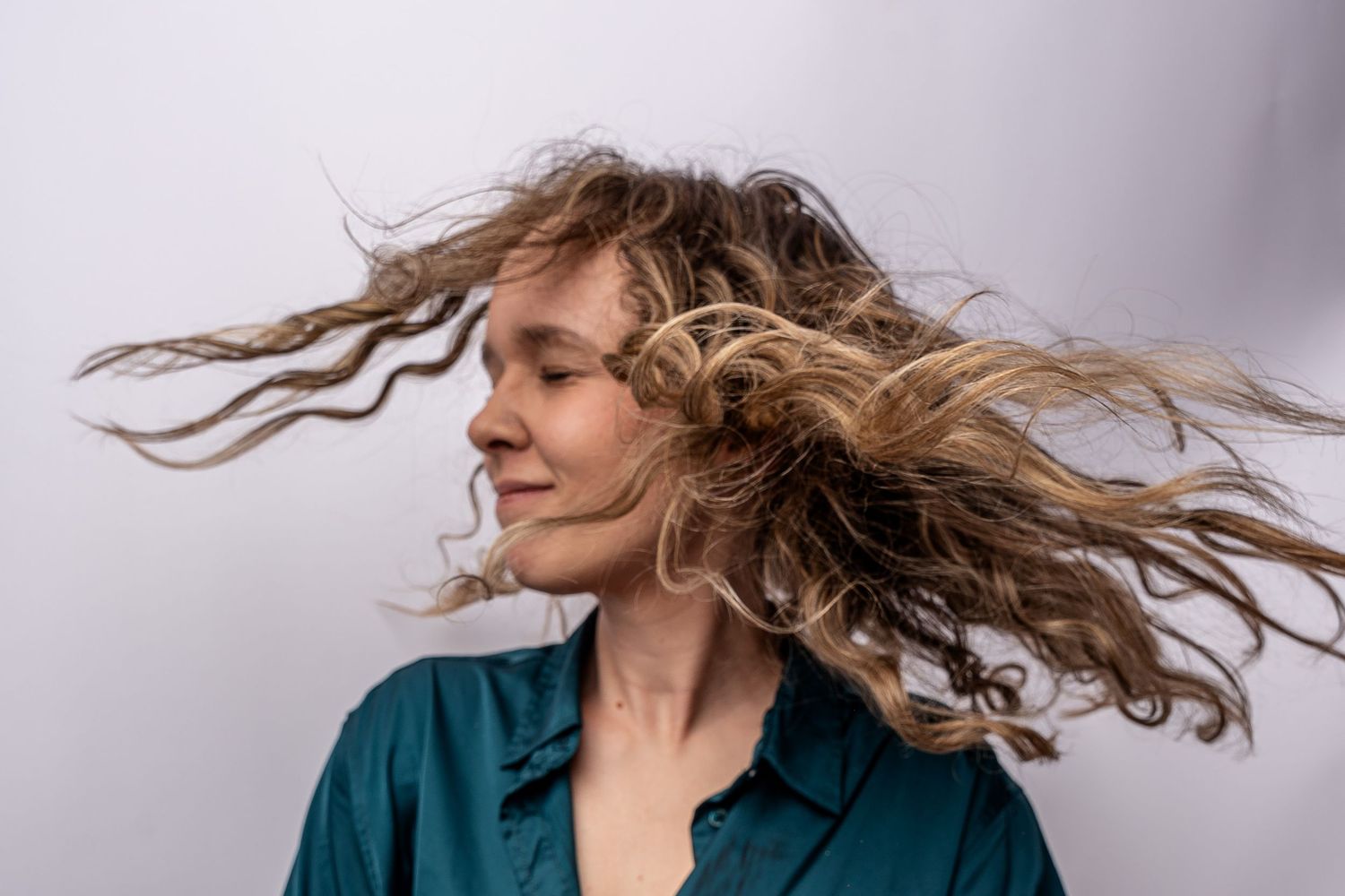 A woman with long wavy hair flowing in the wind poses serenely against a white background.