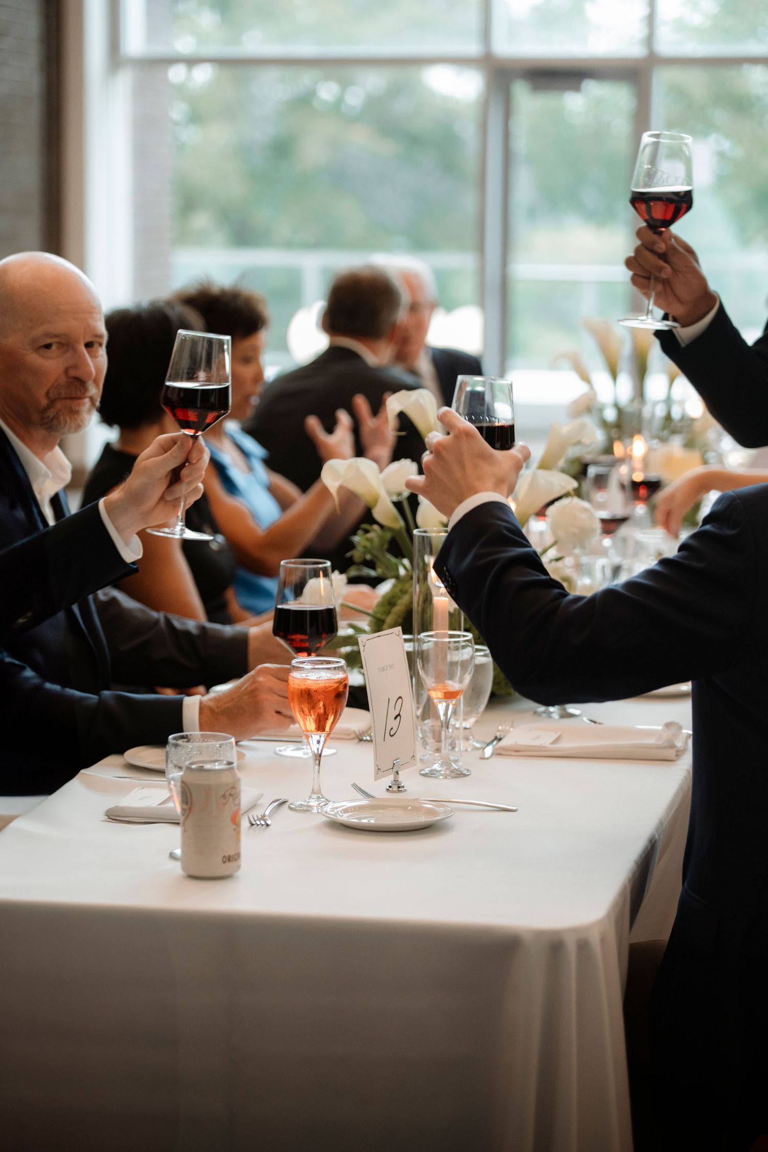 Wedding guests raise glasses of red wine in a toast at an elegant reception dinner table.