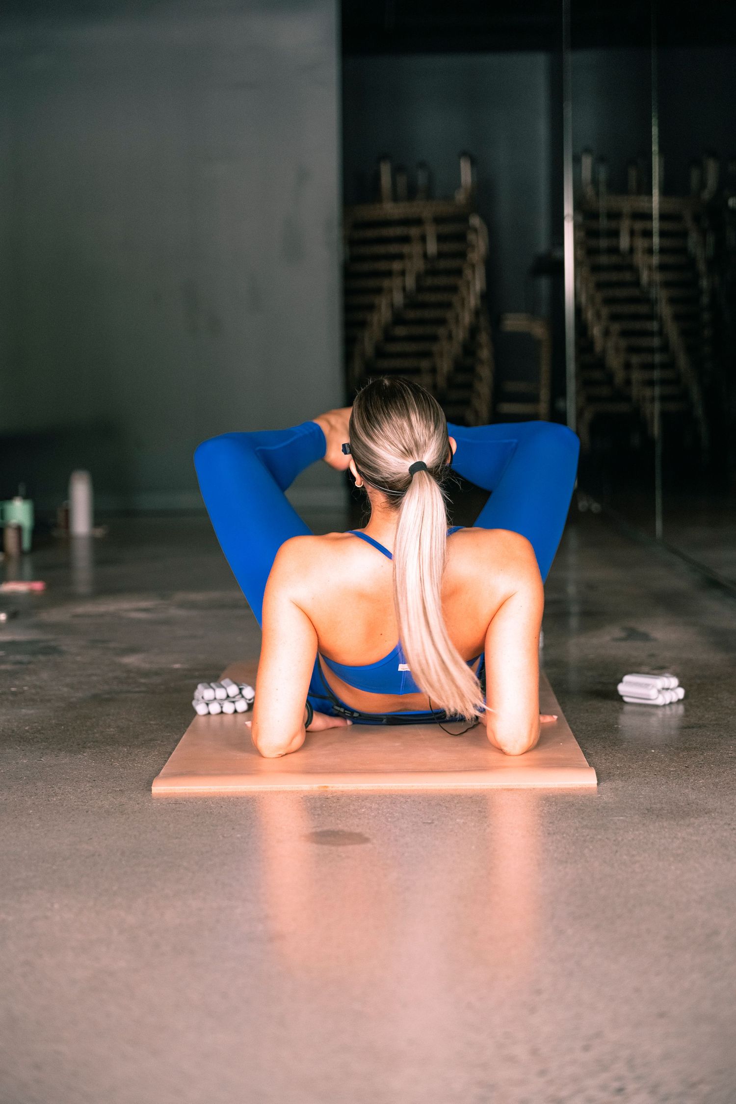 Woman in blue athletic wear doing sit-ups on a mat in a gym, viewed from behind.