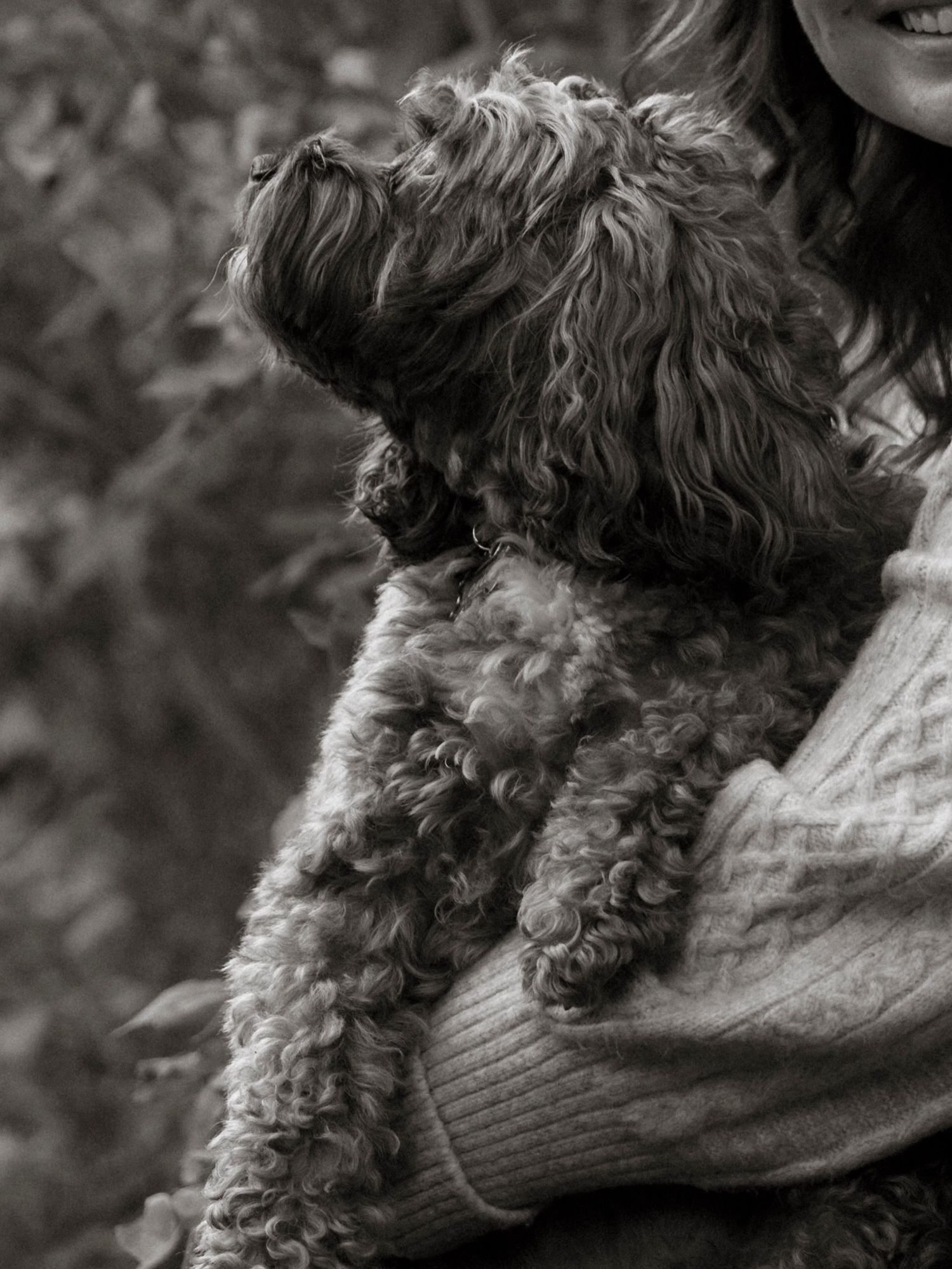 A woman in a knit sweater holds a curly-haired dog in a black and white outdoor portrait. Family and pet photography in Regina Saskatchewan.