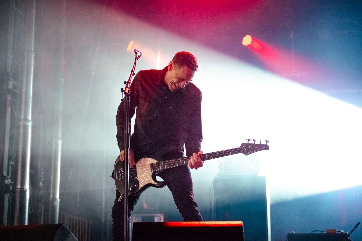 Guitarist performing on stage under dramatic red and white spotlights during a live rock concert.