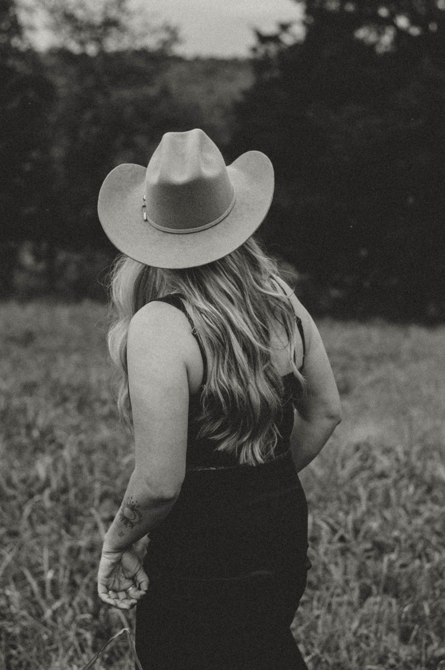 Black and white portrait of someone wearing a cowboy hat in a field.