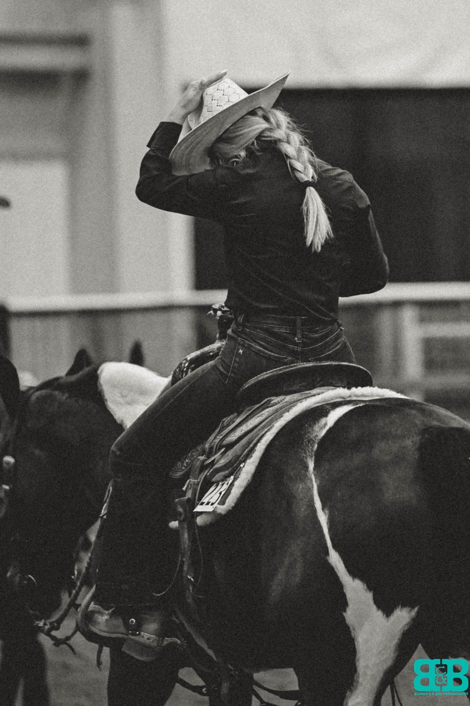 Black and white image of a rider in western attire on a paint horse at a rodeo event.