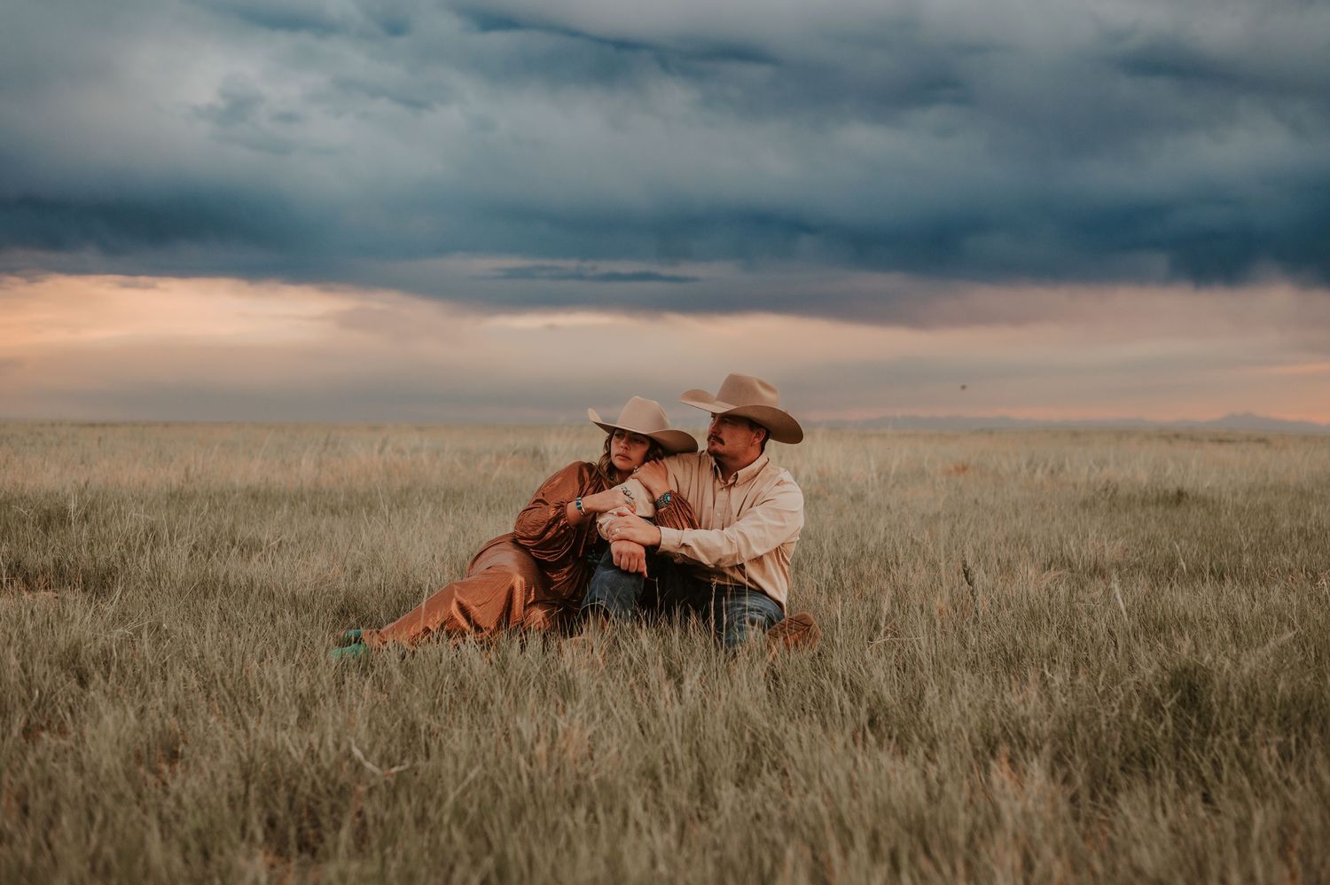 Horses resting in tall prairie grass under moody cloudy skies.