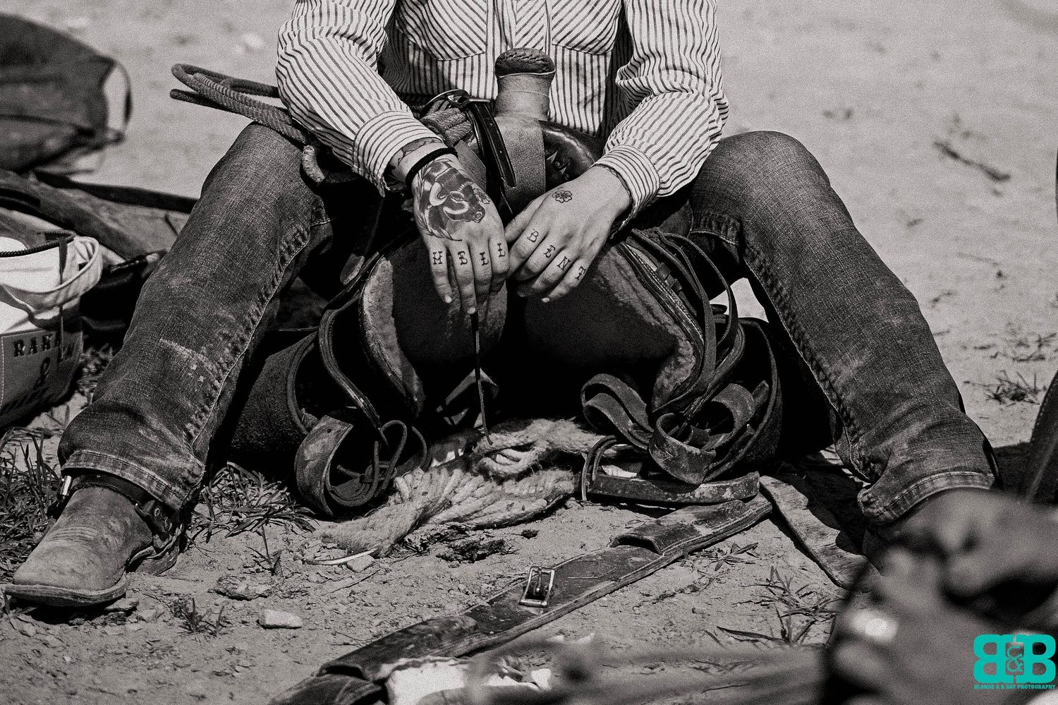 Close-up black and white photo of vintage cowboy boots and chaps on dusty ground.