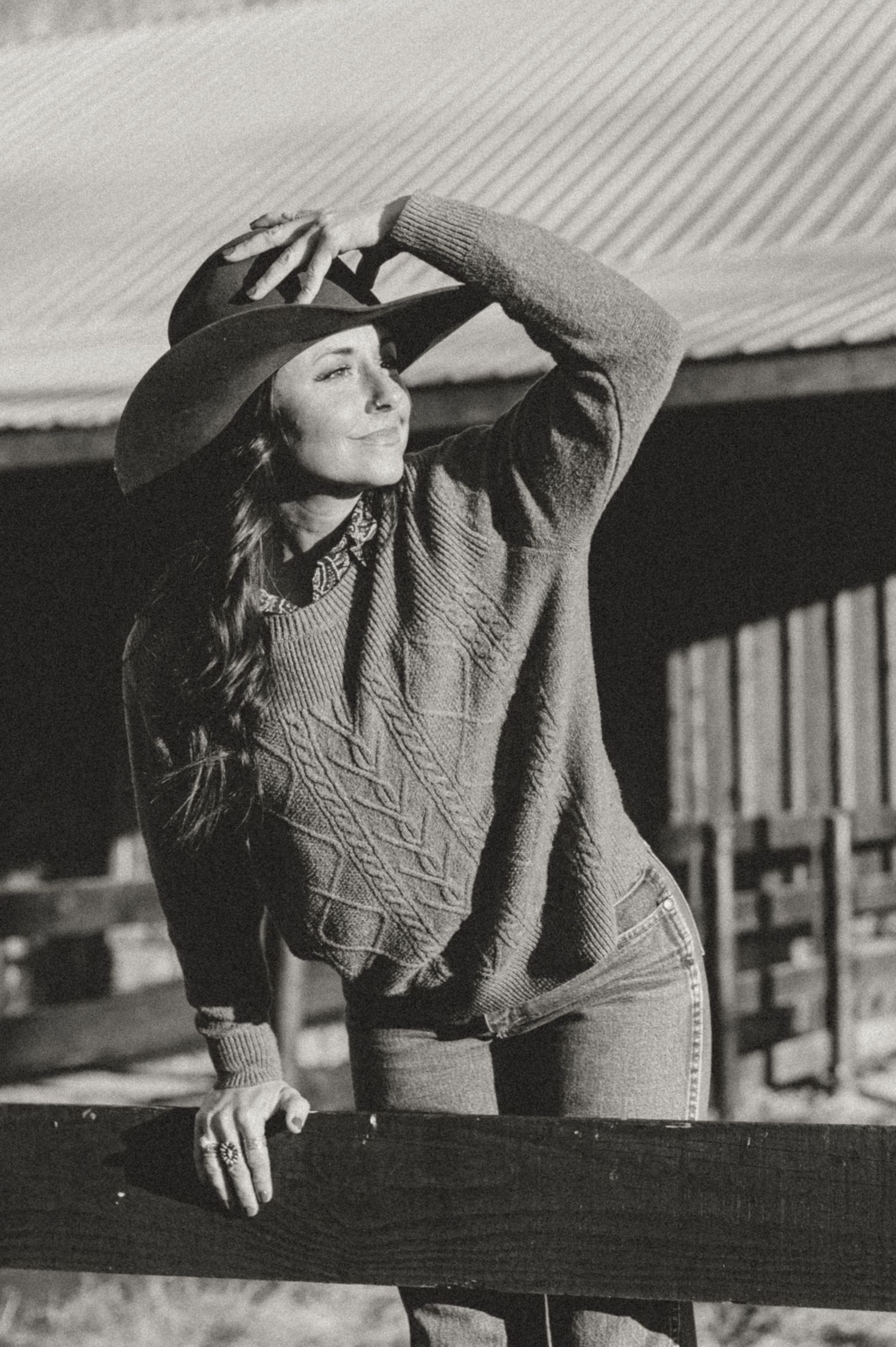 Vintage-style photo of someone in western wear leaning on a wooden fence.