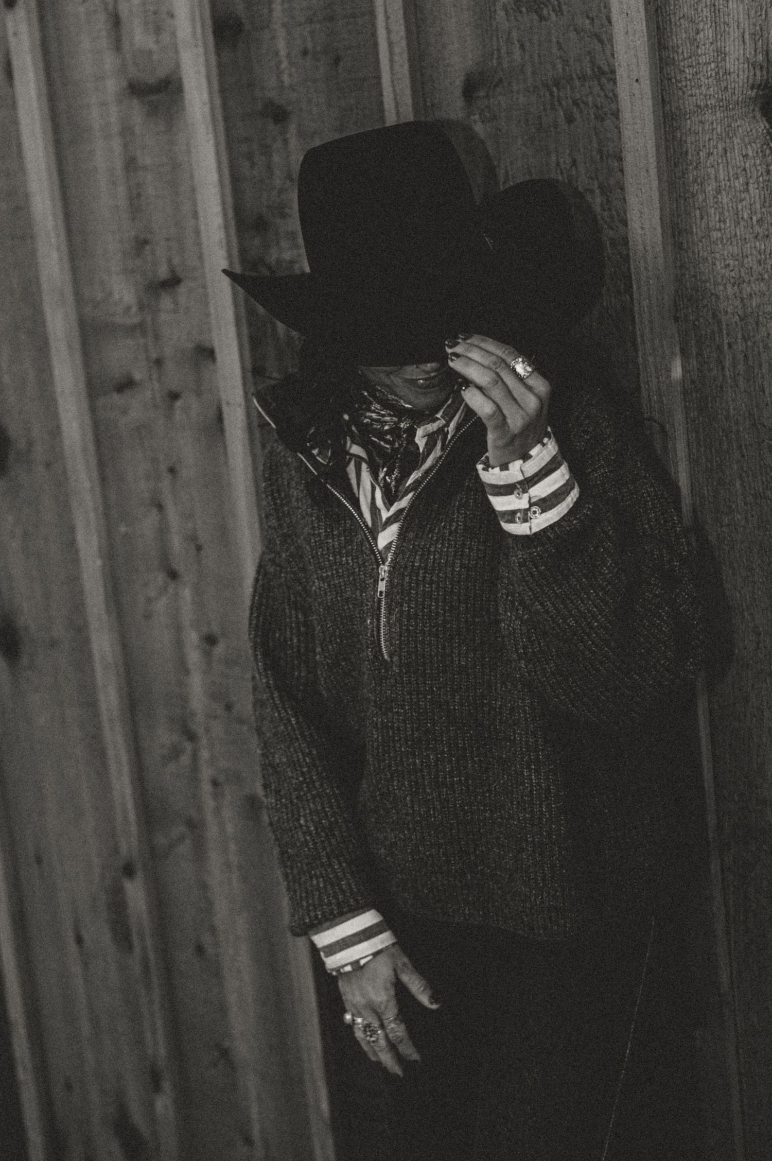 Dark silhouette figures wearing cowboy hats against wooden barn wall.