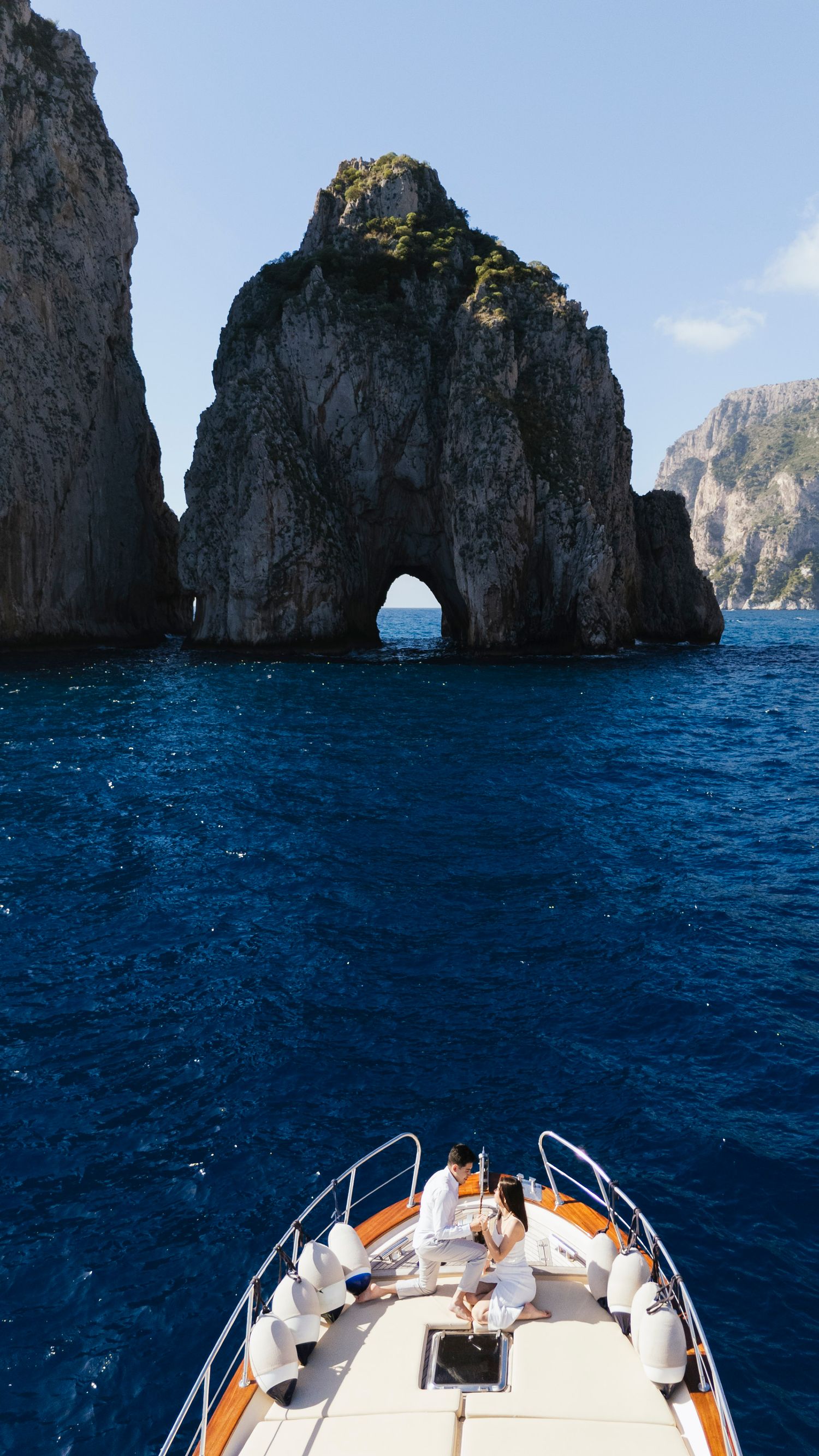 Boat approaching dramatic rocky cliffs rising from deep blue Mediterranean waters near Capri Island.