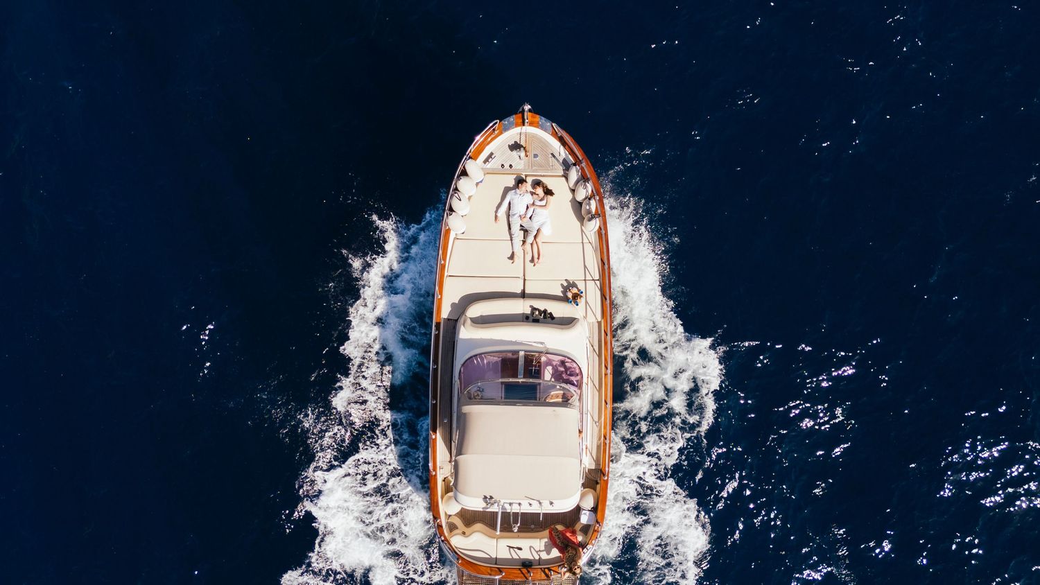 A luxury yacht cruises through blue ocean waters creating a dramatic wake pattern behind it.