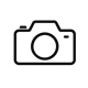 Simple black and white camera icon with lens, viewfinder, and shutter button outline on white background.