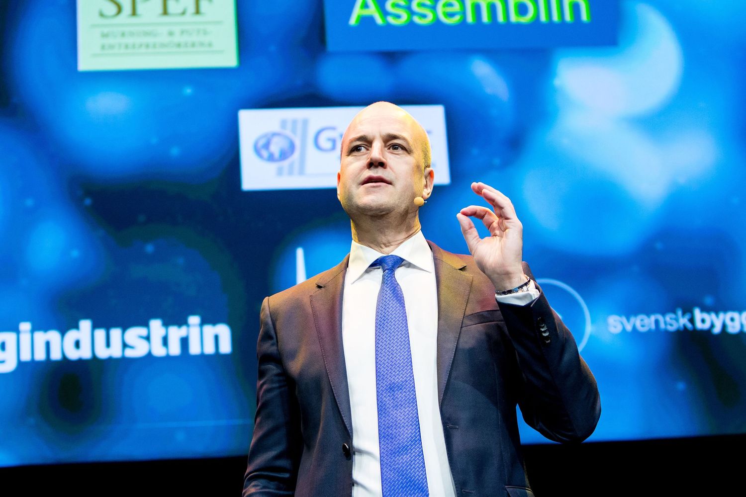 Man in suit gesturing while speaking on stage at a Swedish construction industry conference.