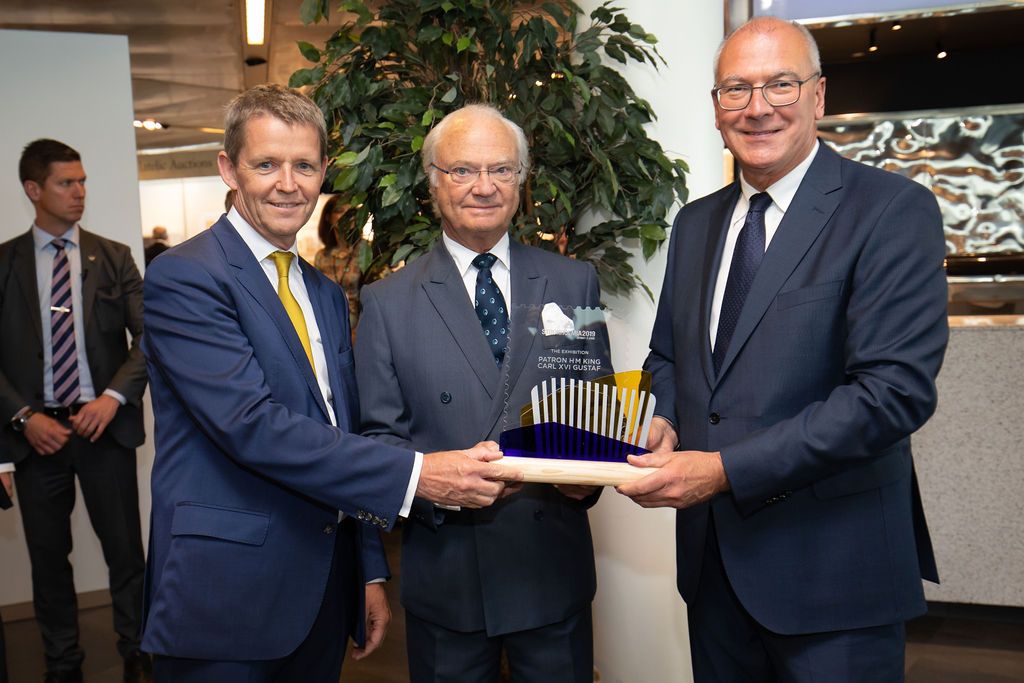 Three businessmen in suits presenting a crystal award trophy at a formal corporate ceremony.