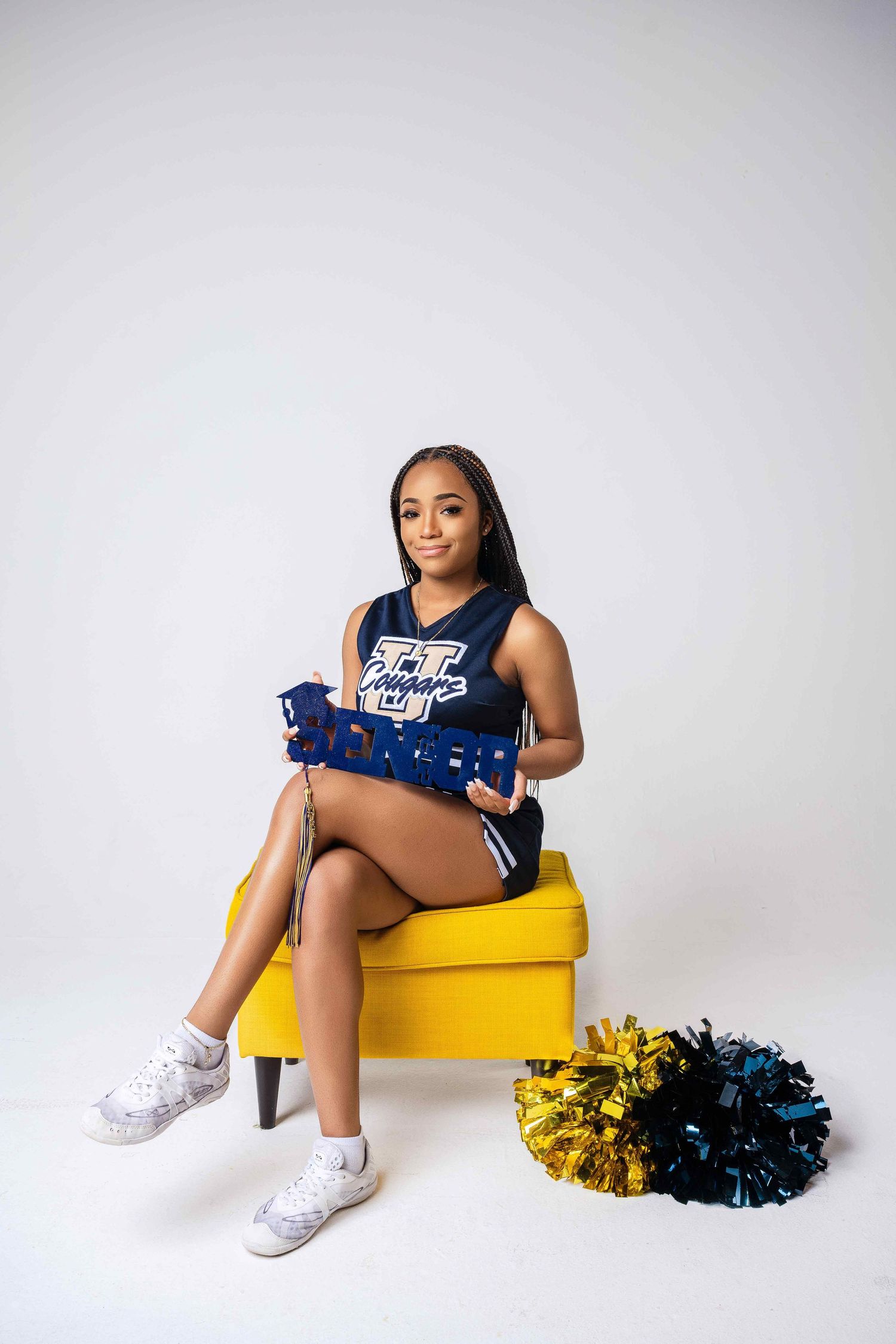 Cheerleader in blue uniform poses on yellow box with pom poms.