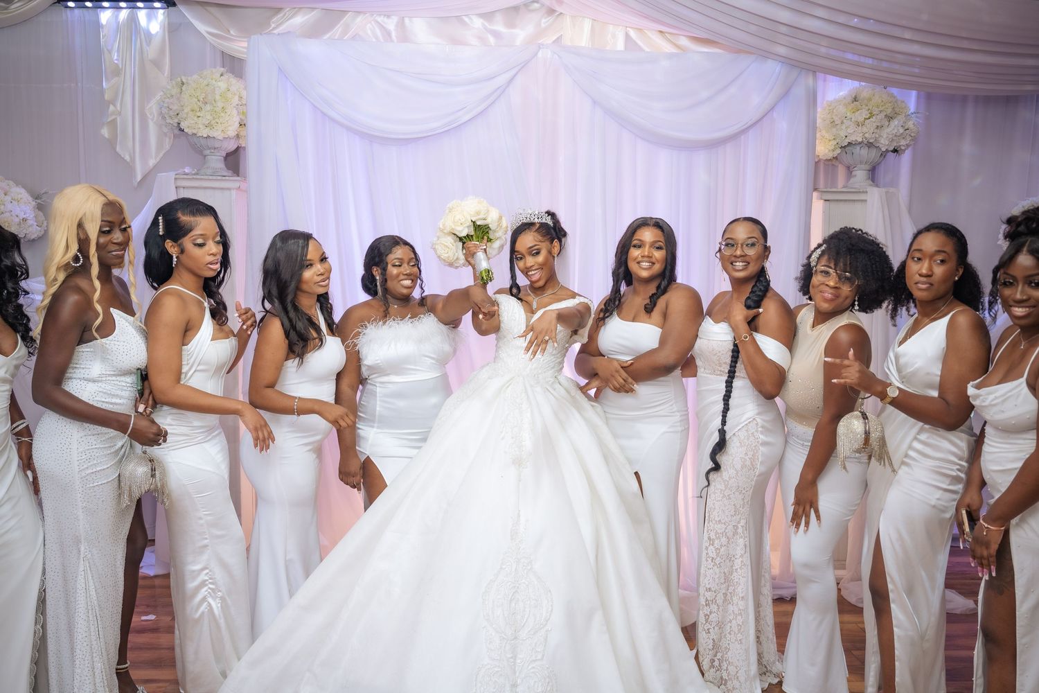 A bridal party in white dresses poses together under elegant white draping at a wedding reception.