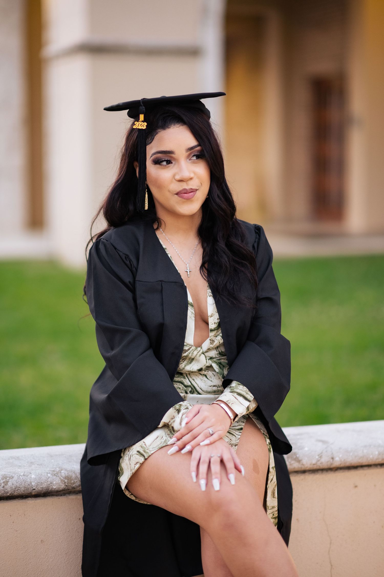 Graduate in cap and gown poses on stone ledge near campus architecture.
