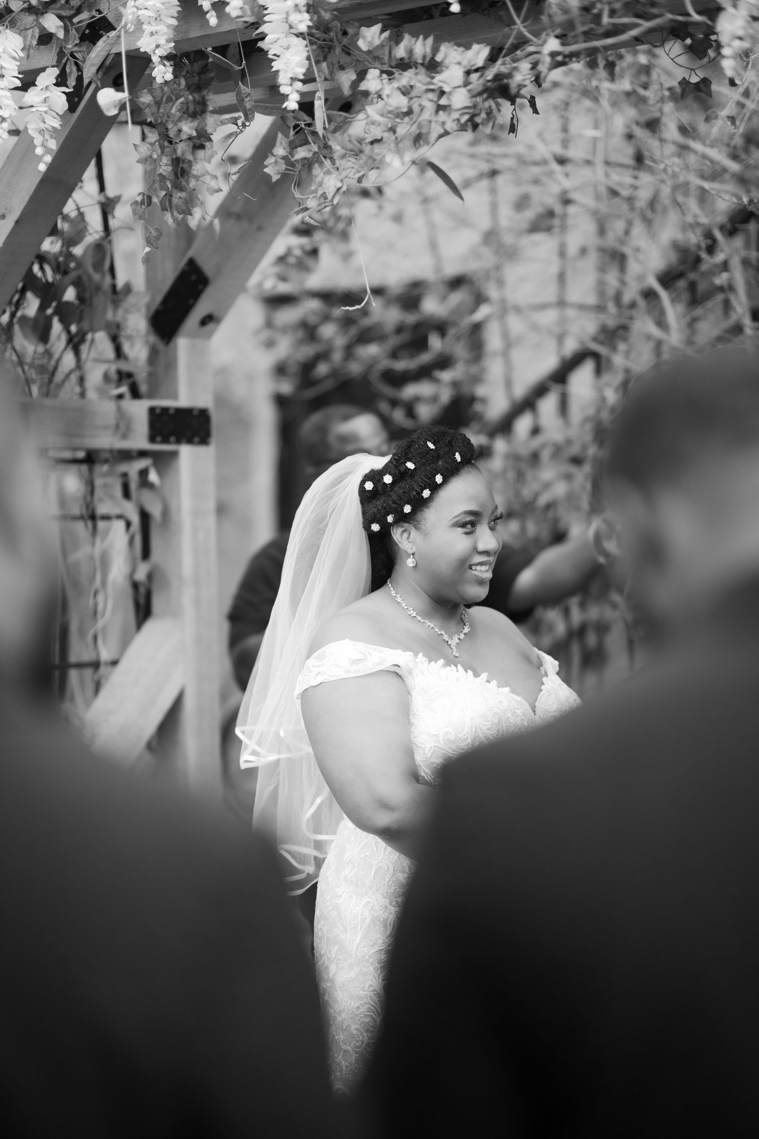 A black and white photo shows a bride smiling during her outdoor ceremony.