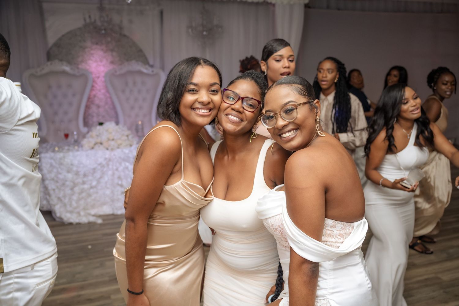Wedding guests in cream-colored dresses share a joyful moment on the dance floor.