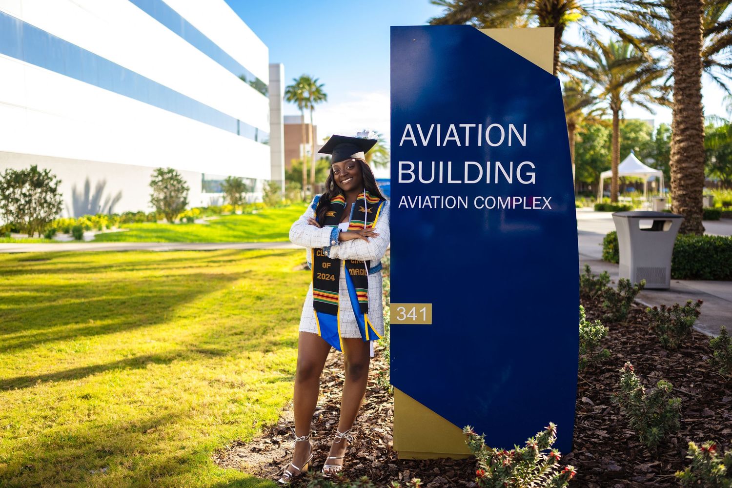 Graduate standing in front of Aviation Building sign with palm trees in background.
