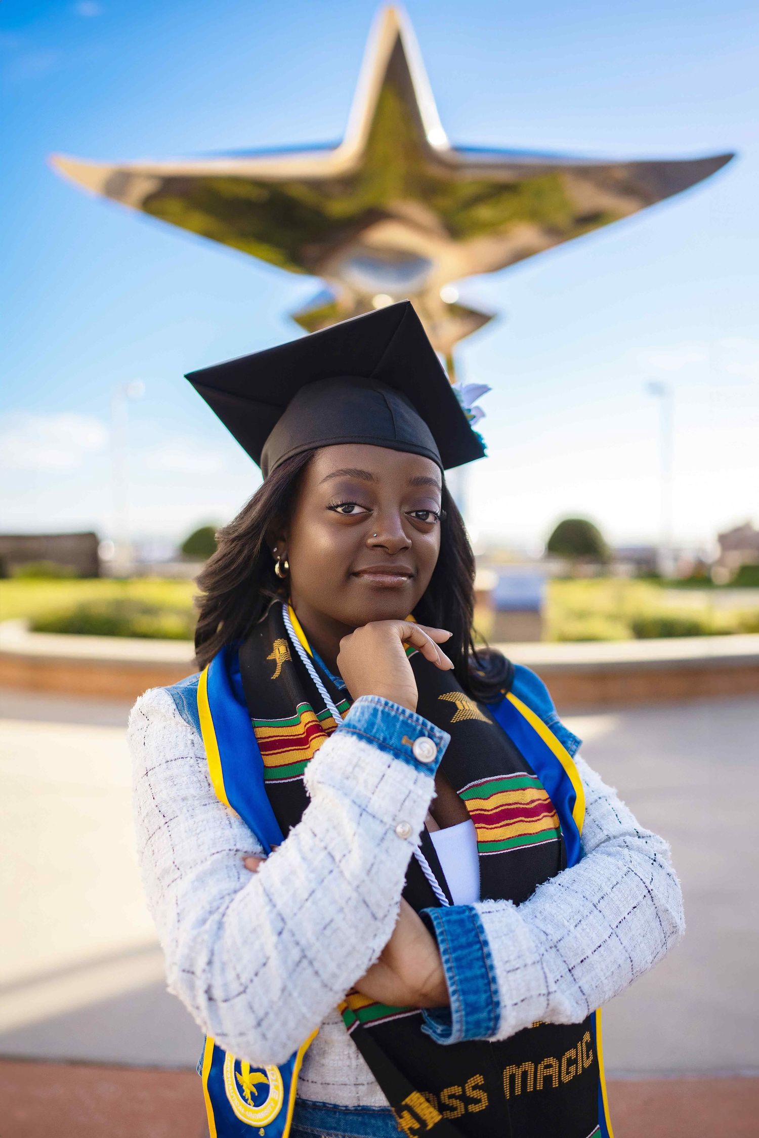 Graduate in academic regalia and colorful stole poses confidently in front of golden star monument.