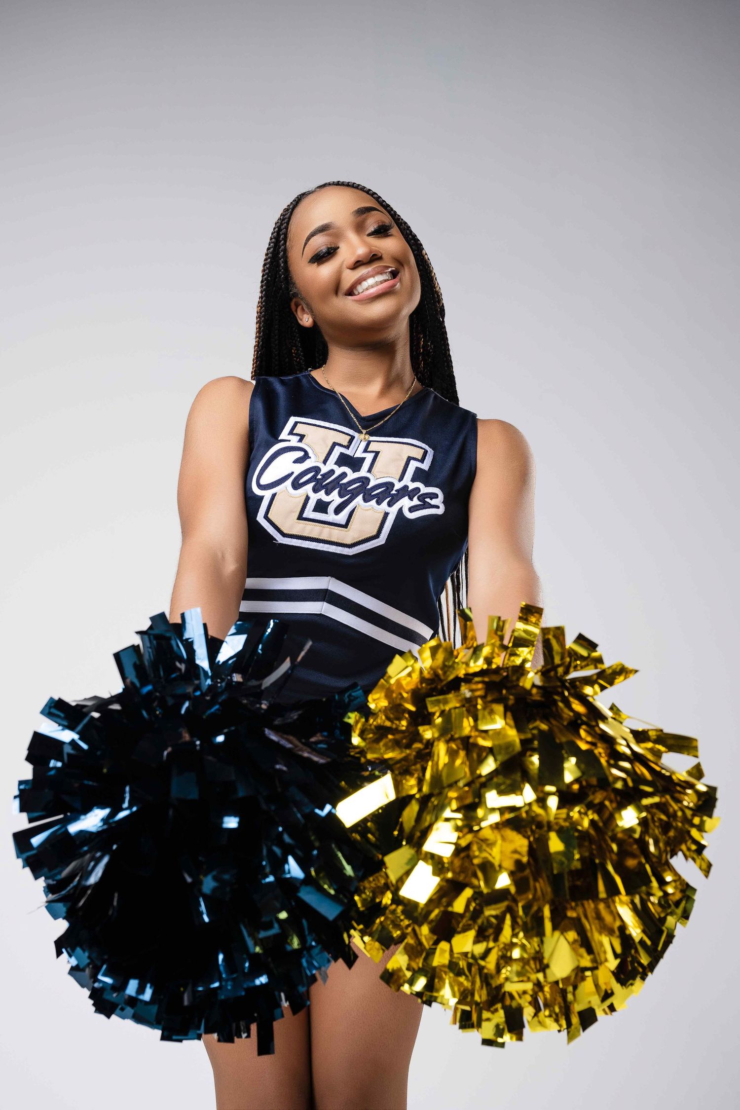 Cheerleader holding blue and gold pom poms in navy uniform against white backdrop.