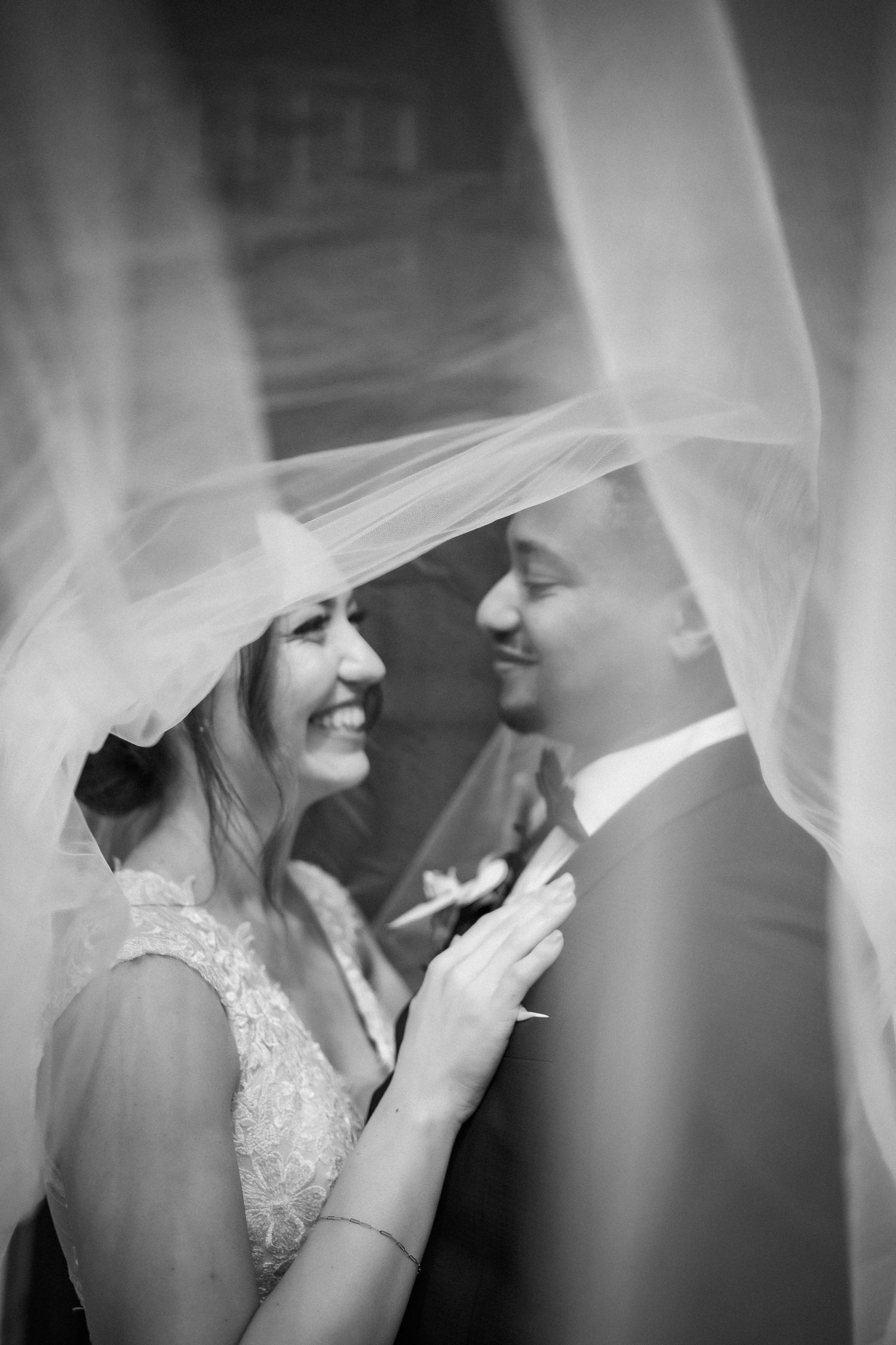 A black and white photo of a couple sharing an intimate moment under a wedding veil.