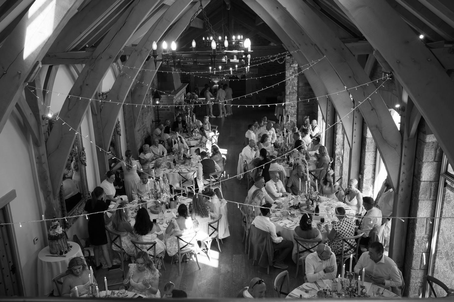 Black and white aerial view of elegant barn wedding reception with guests seated at round tables under string lights.