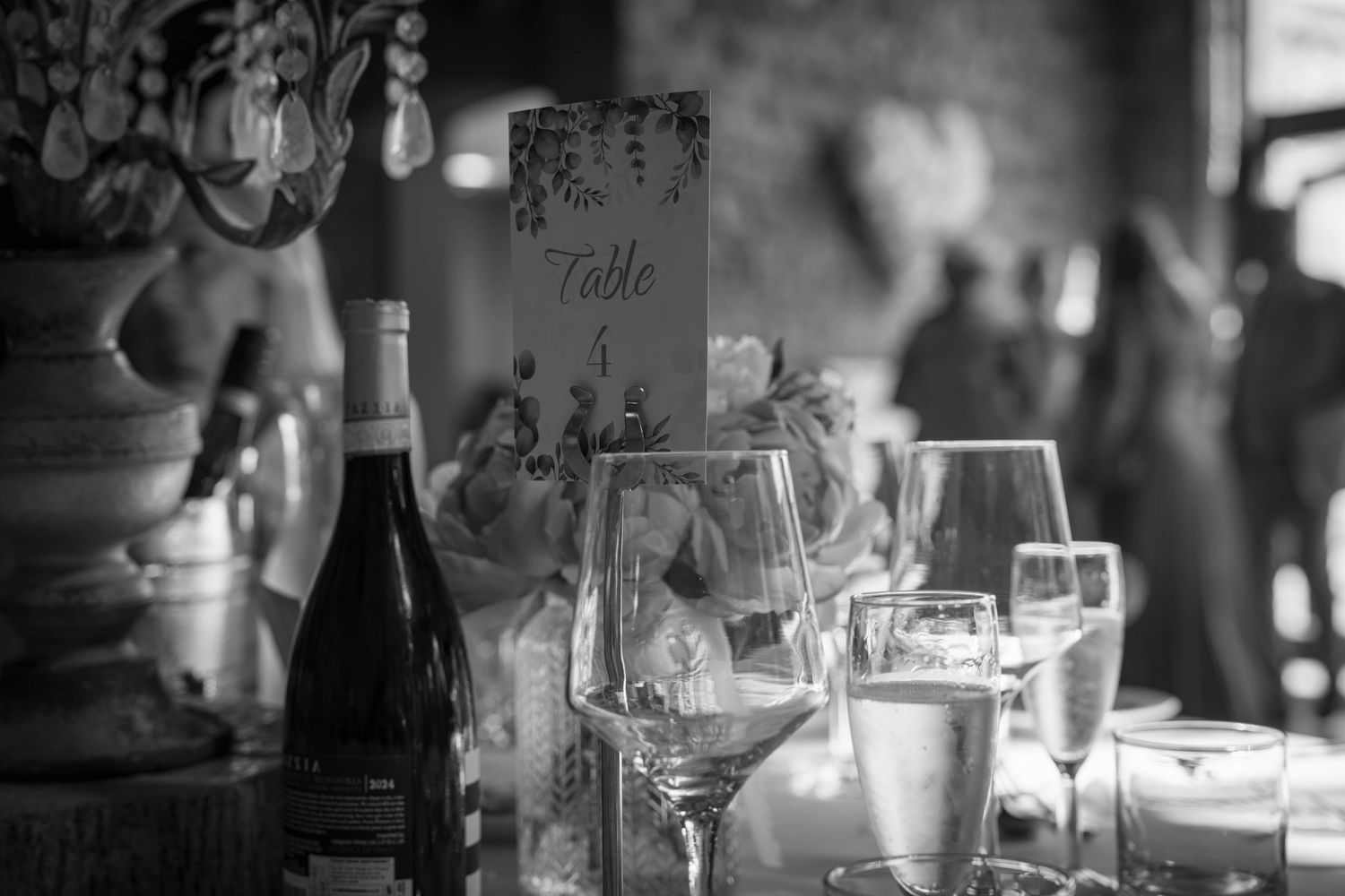 Black and white wedding reception table with wine bottle, glasses, and elegant Table 4 sign centerpiece.