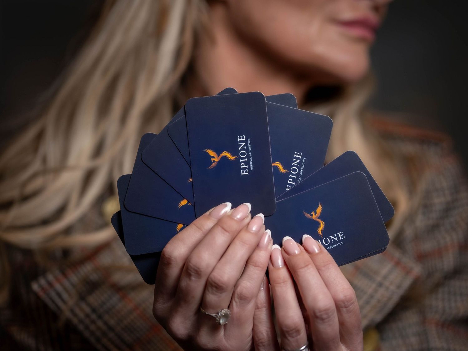 Multiple hands hold playing cards with blue backs in a fanned out arrangement against a dark background.