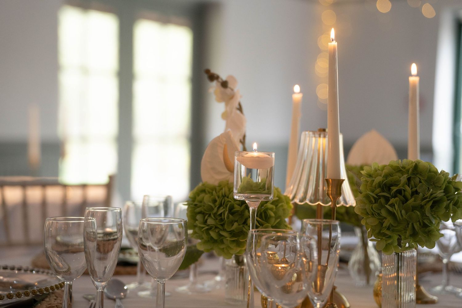 Elegant wedding table setting with green floral centerpieces, tall candles, and crystal glassware on a decorated dining table.