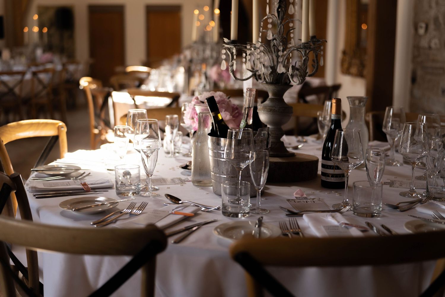 Elegantly set round wedding reception table with crystal glassware, candelabra centerpiece, and white linens in a dimly lit venue.