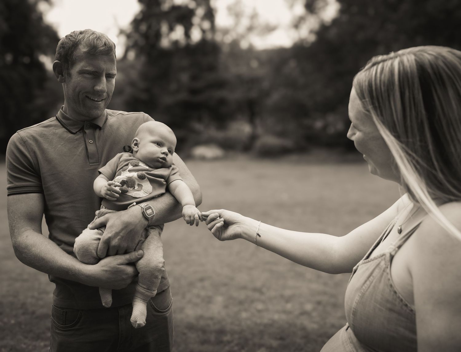 A series of black and white photos showing tender moments between parents and their baby outdoors in a field.