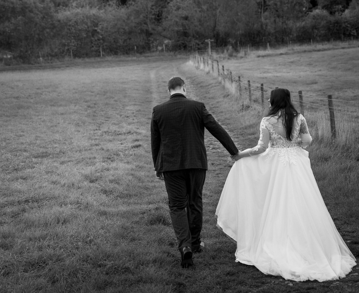Couple walking through a countryside field in formal wedding attire.