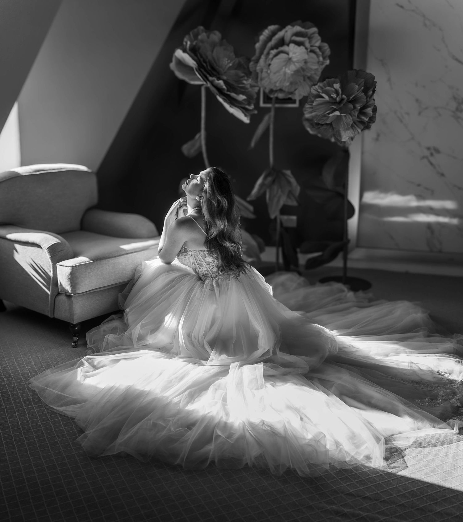 Black and white photo of a bride in a flowing tulle gown seated on the floor in an elegant room.
